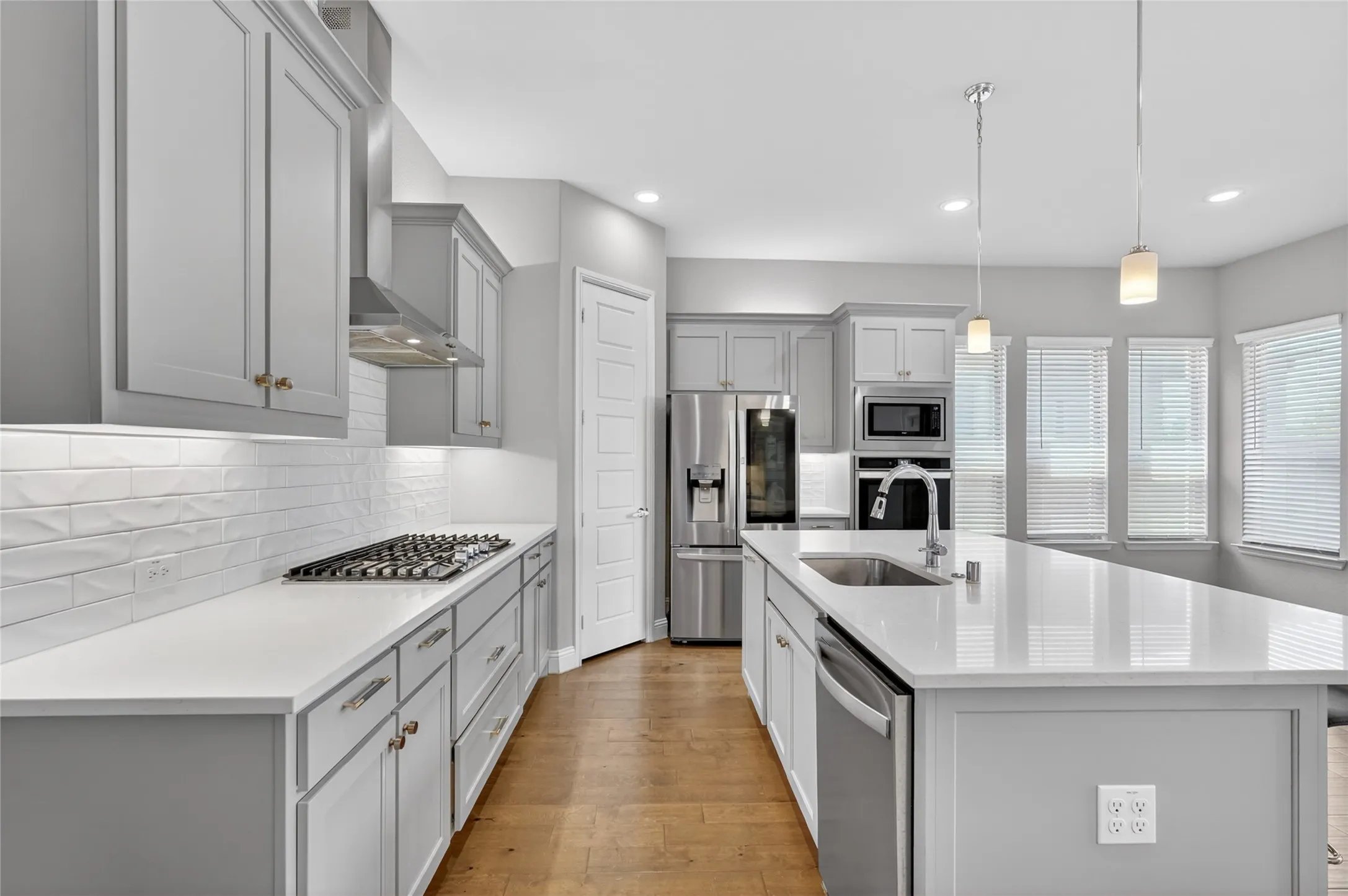 Open-concept kitchen featuring extensive light gray cabinetry, stainless steel appliances, white subway tile backsplash, and wood-finish flooring