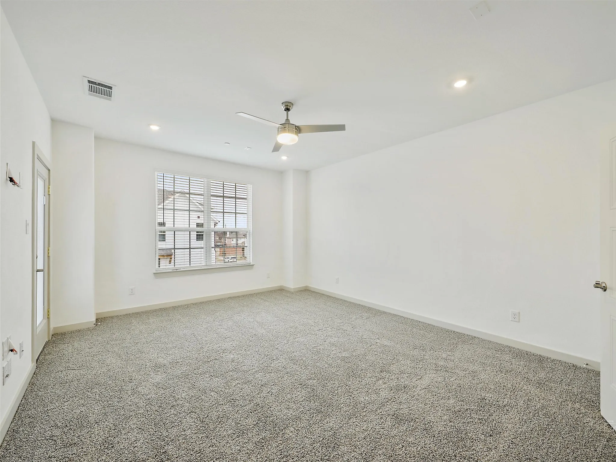 Spacious room featuring neutral carpeting, a large window with horizontal blinds, a ceiling fan, and recessed lighting