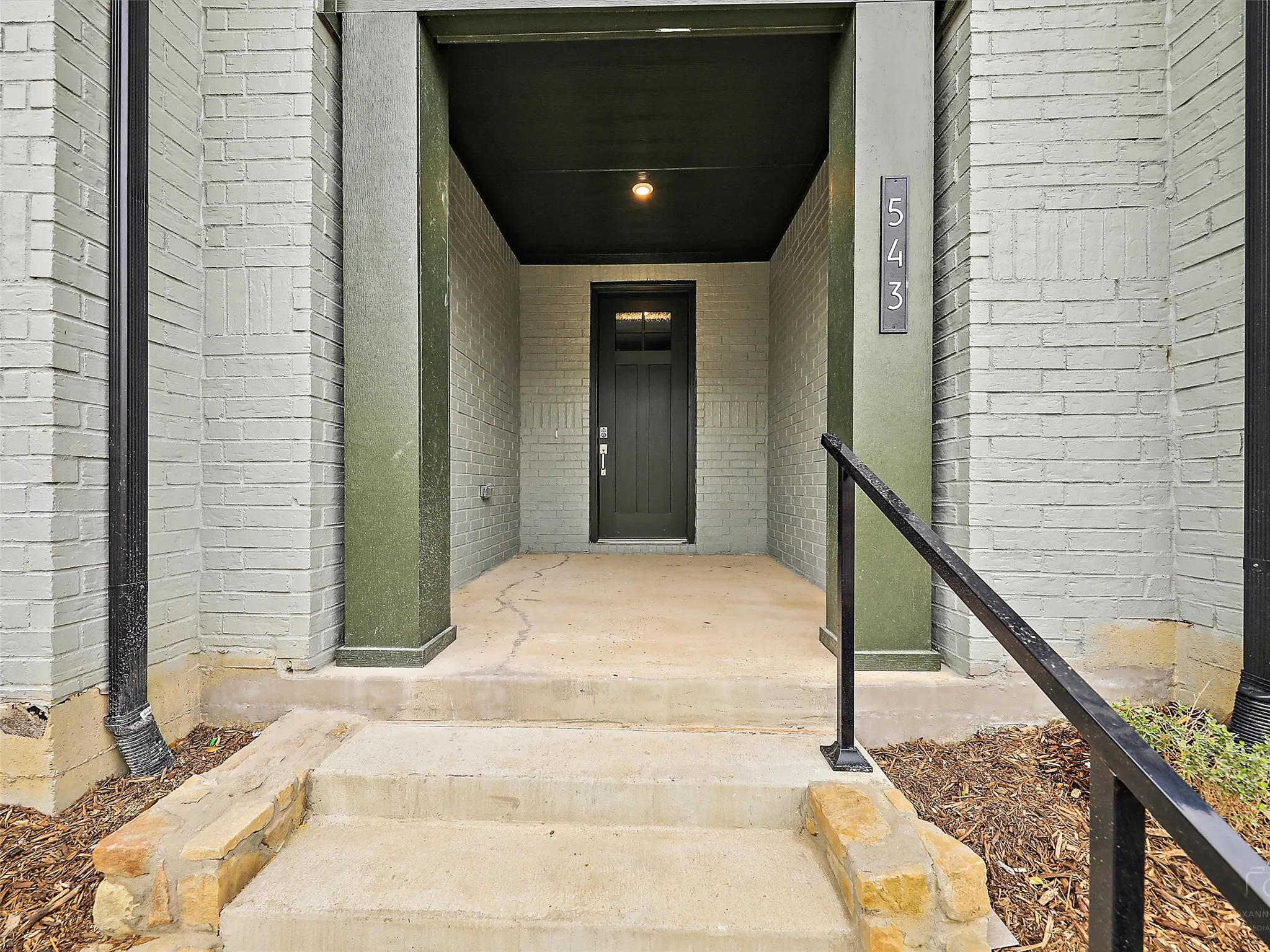 Inviting entryway featuring light-colored brick exterior, dark green trim, and a prominent front door