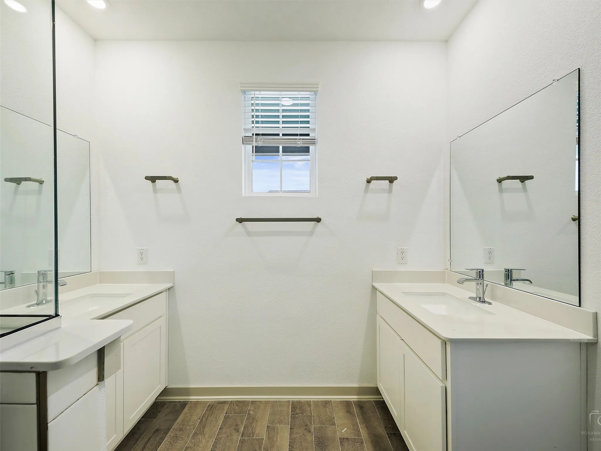 Dual white vanities with integrated sinks and chrome fixtures, illuminated by recessed ceiling lights