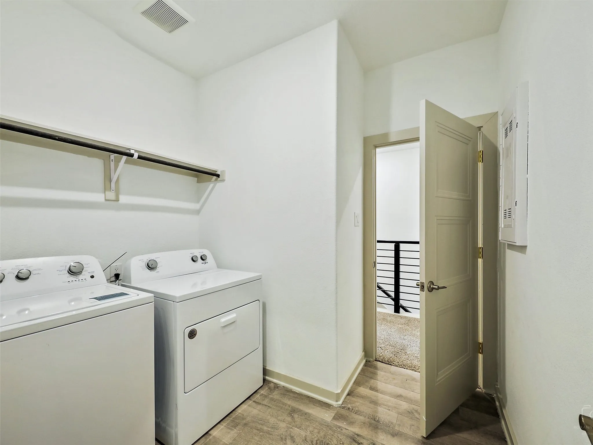 Dedicated laundry space featuring a white washer and dryer, wood-finish flooring, and overhead shelving with a hanging rod