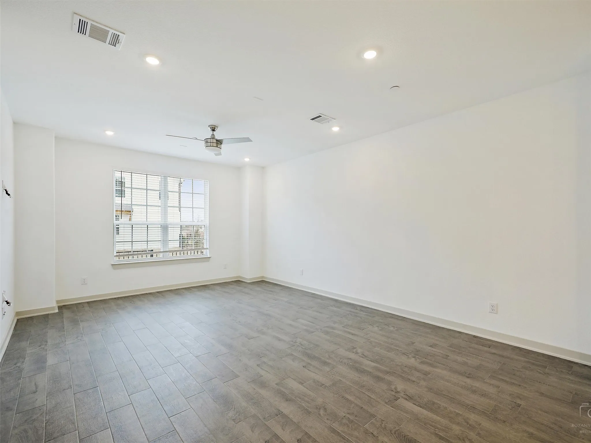 Spacious interior featuring a large window with white blinds, recessed lighting, a ceiling fan, and wood-finish flooring