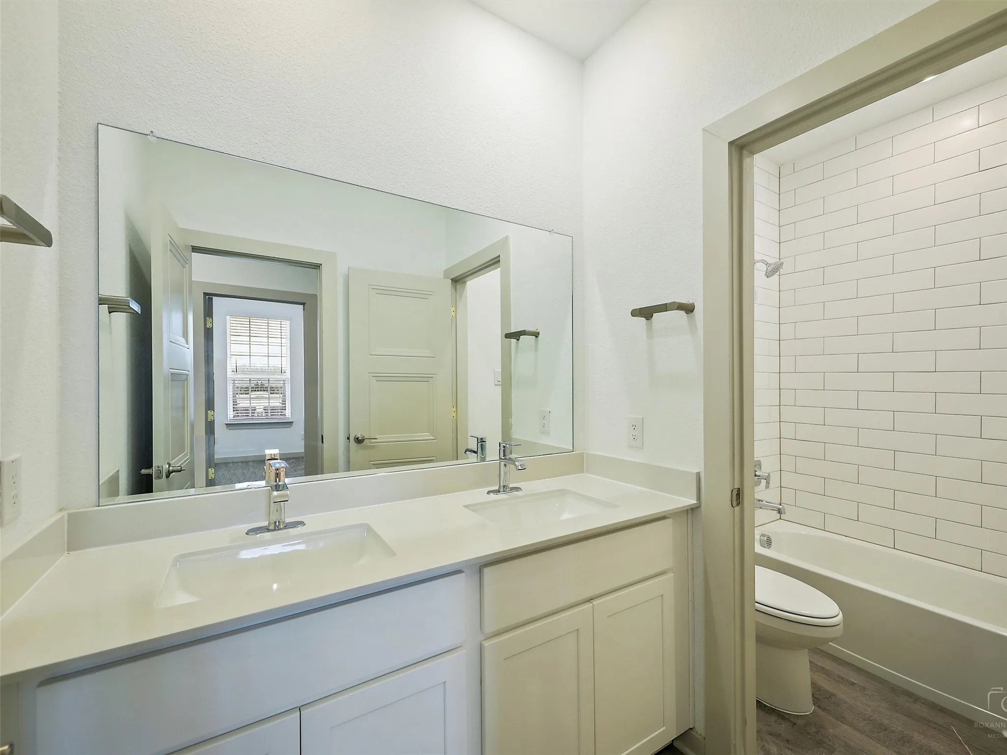 Bathroom featuring a double vanity with white cabinetry and integrated sinks, a wide frameless mirror, and a shower-tub combination with white subway tile surround