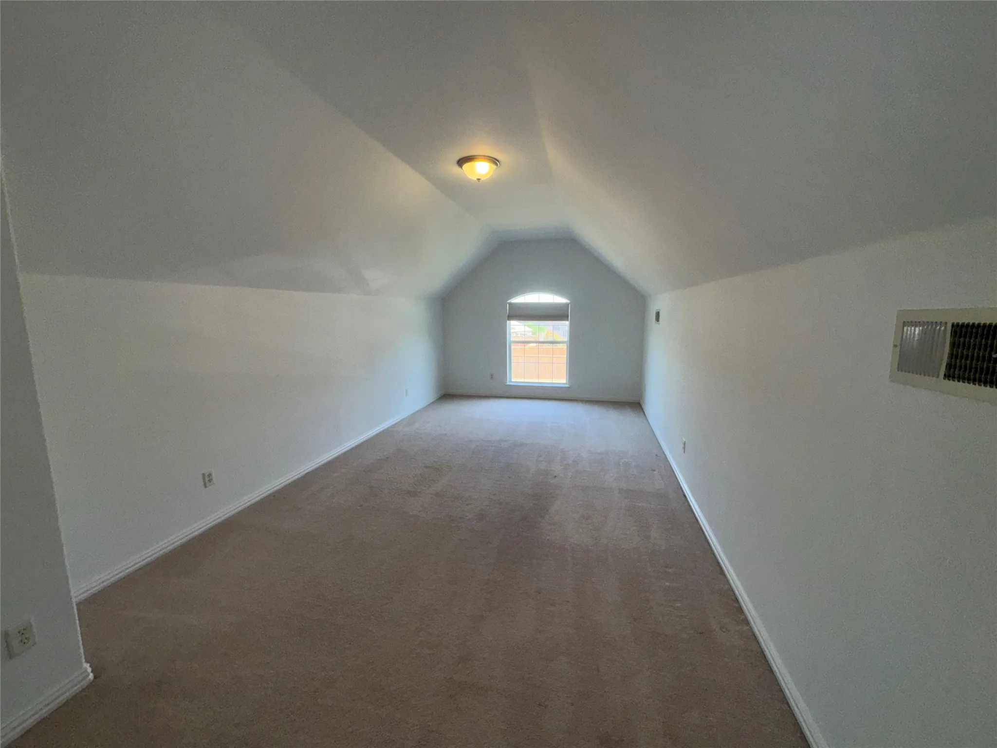 Spacious upper-level bedroom featuring vaulted ceilings, recessed lighting, and abundant natural light from a front-facing window