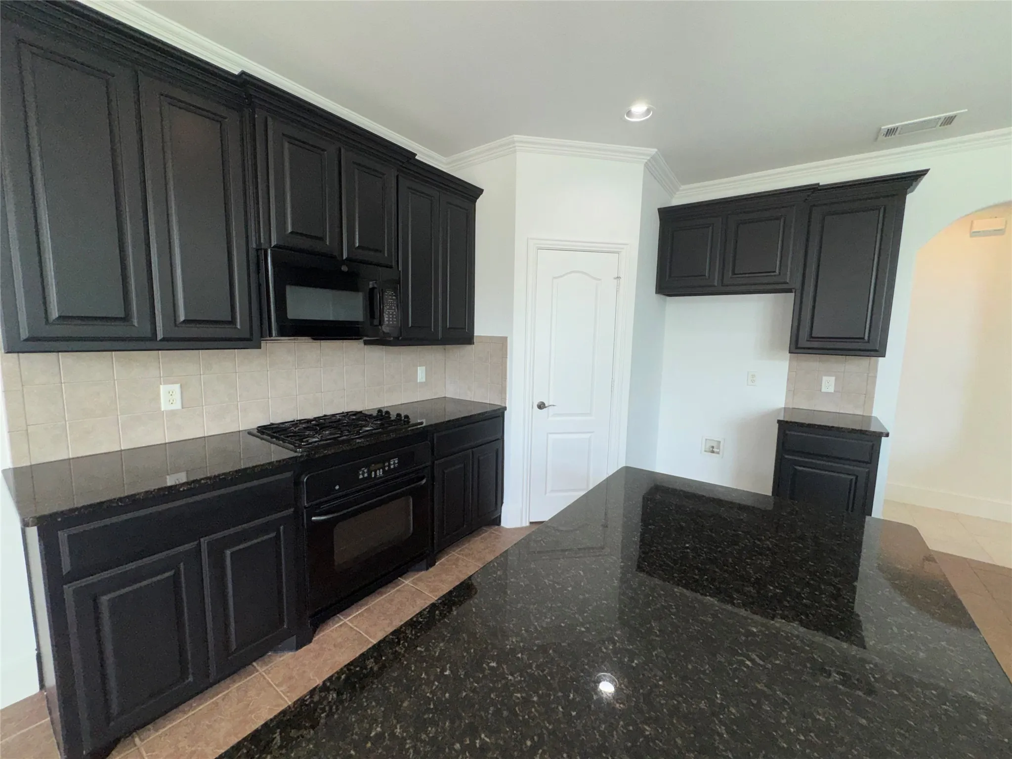 Modern kitchen featuring dark cabinetry with recessed panel detailing, stainless steel gas range and built-in microwave, subway tile backsplash, and a spacious dark stone countertop with waterfall edge