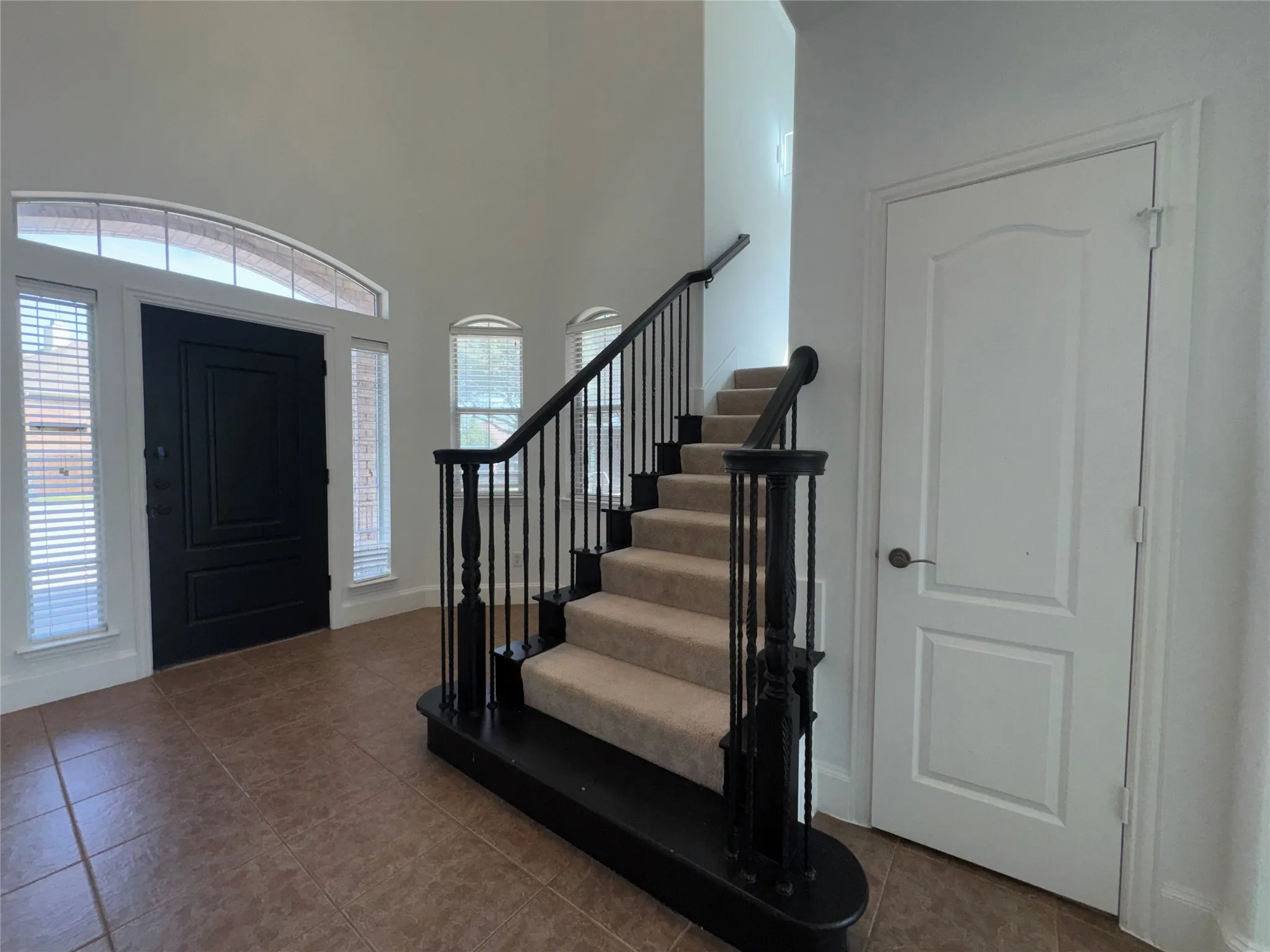 Two-story foyer with tile flooring and a grand staircase featuring dark wood newel posts and wrought iron balusters