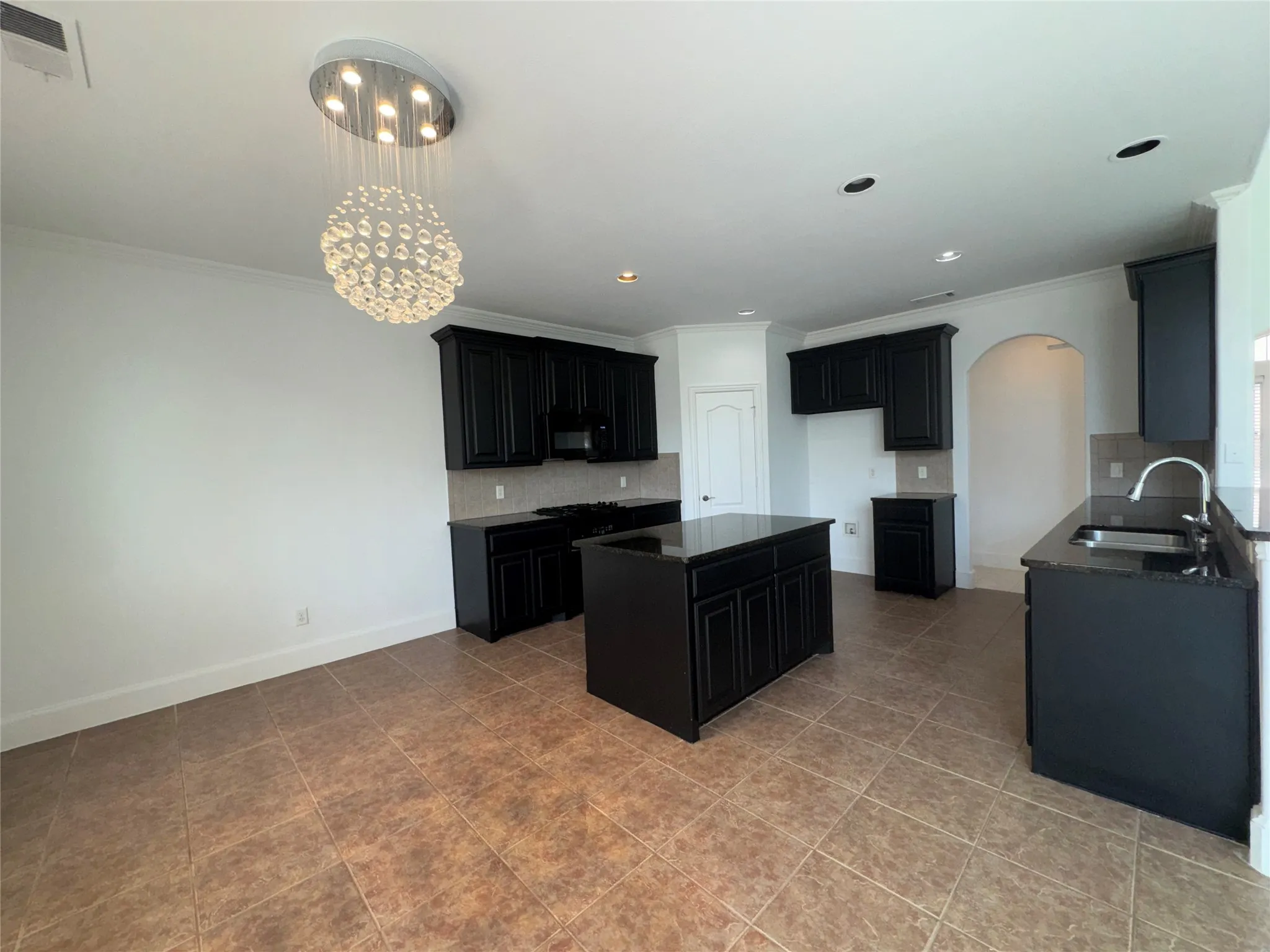 Spacious kitchen featuring black cabinetry, a large center island with seating, stainless steel appliances including a professional-style range, and cork-finish flooring throughout