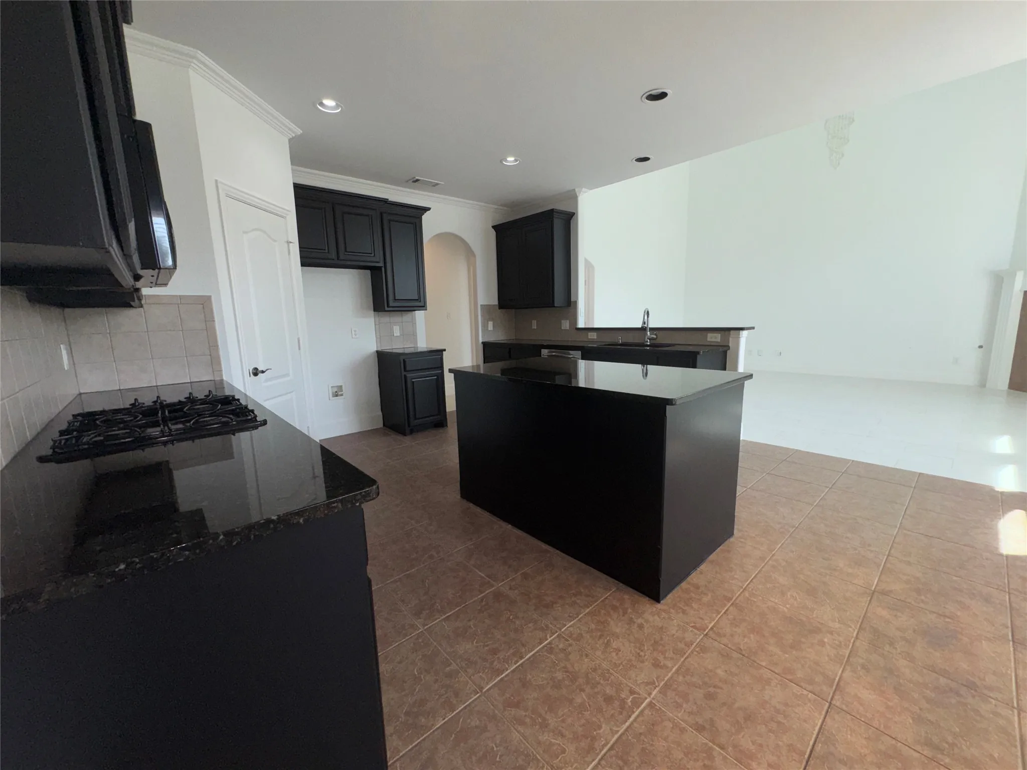 Modern kitchen featuring a substantial black island with waterfall edge, gas cooktop with stainless steel range hood, dark cabinetry, subway tile backsplash, and wood-finish flooring throughout the open layout