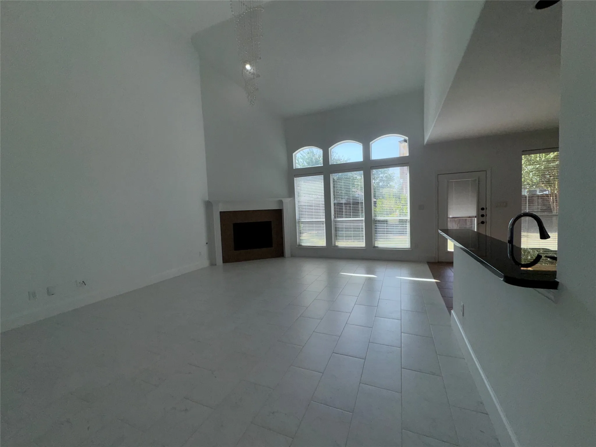 Bright, open living space featuring soaring vaulted ceilings, large multi-pane glass doors flooding the room with natural light, and neutral tile flooring