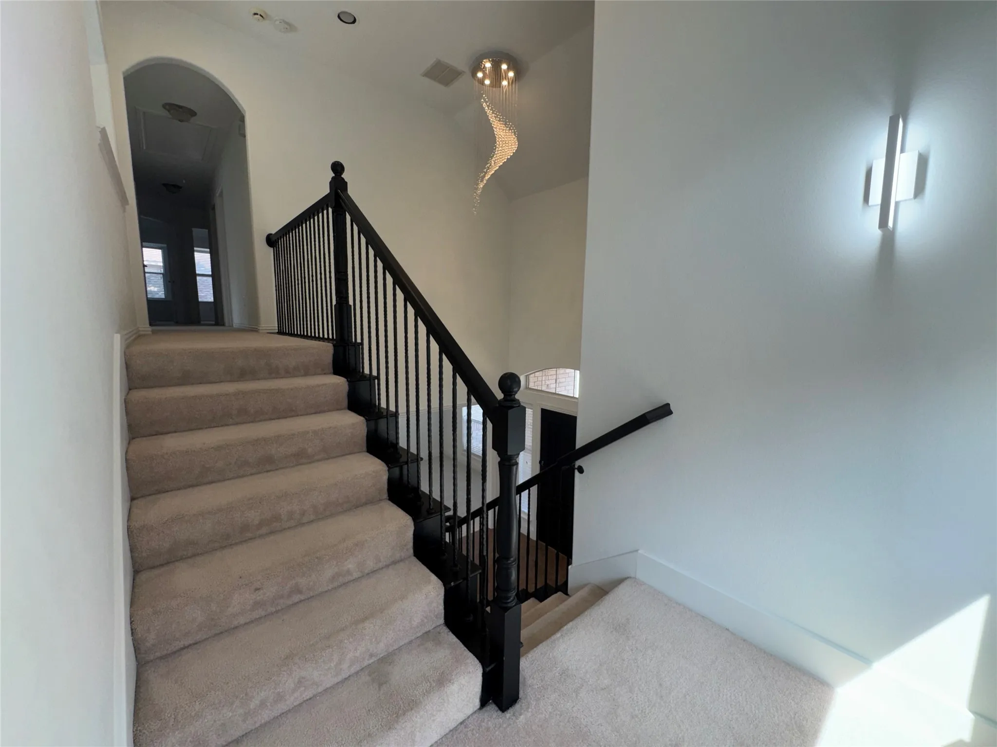 Elegant staircase featuring neutral-toned carpeted treads, black metal railings with turned balusters, and a gracefully arched architectural entryway