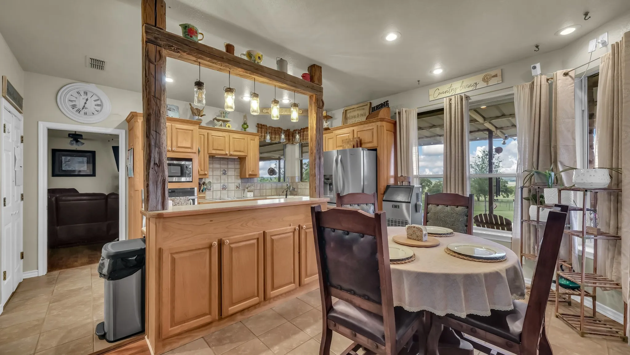 Open-concept kitchen and dining area featuring warm wood cabinetry, a breakfast bar with pendant lighting, integrated stainless steel appliances, and large windows overlooking the exterior