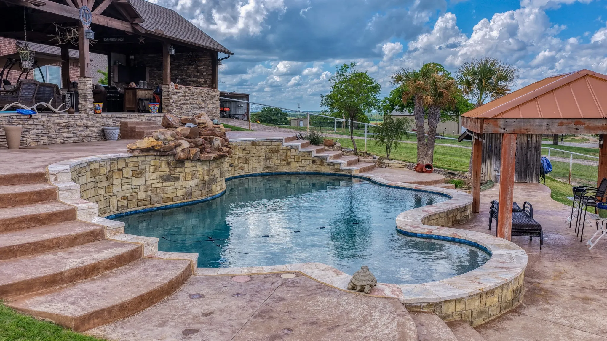 Freeform swimming pool featuring stacked stone walls and a rock waterfall