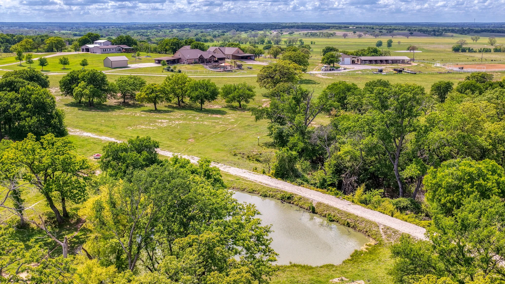 Expansive rural property featuring a large residence, additional structures, and a pond