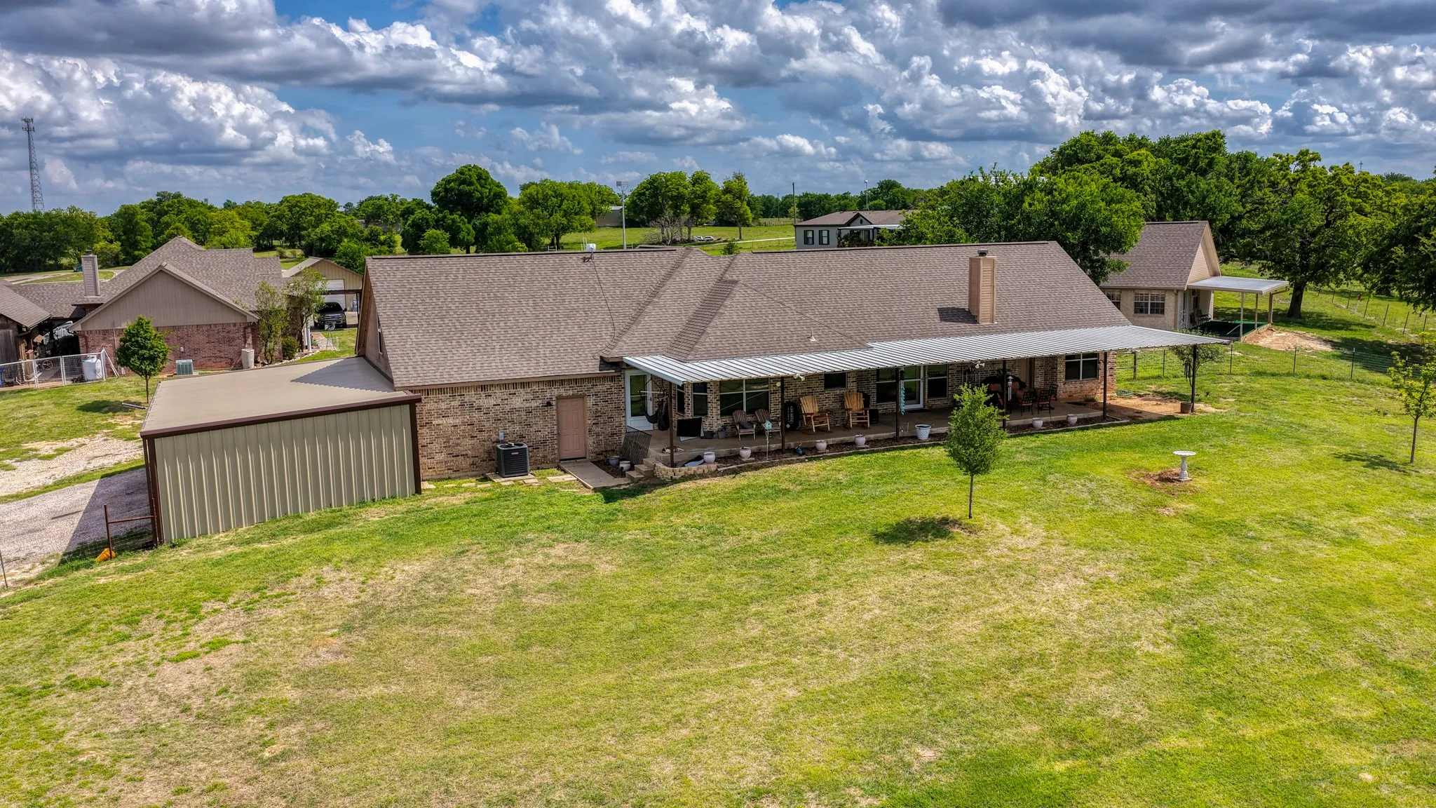 Expansive property featuring a brick and stone exterior residence with a full-length covered porch, an attached metal-sided structure, and an additional detached outbuilding