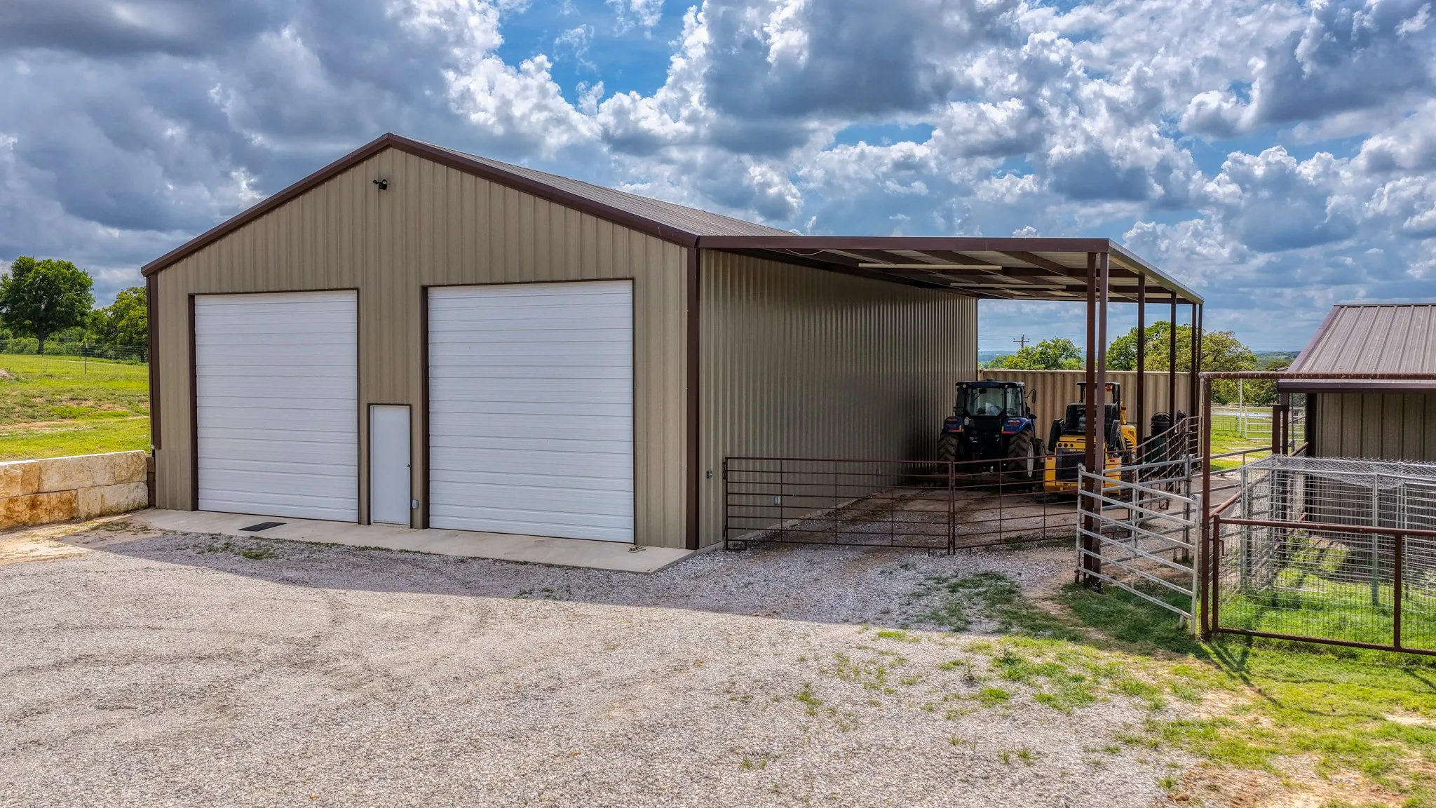 Metal outbuilding featuring two overhead garage doors, a pedestrian door, a covered lean-to, and an additional smaller metal structure