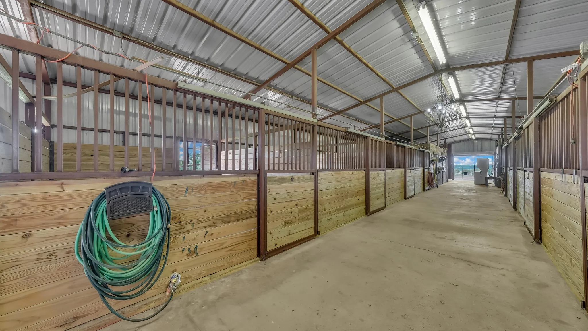 Spacious barn interior featuring multiple stalls with wood paneling and metal grating