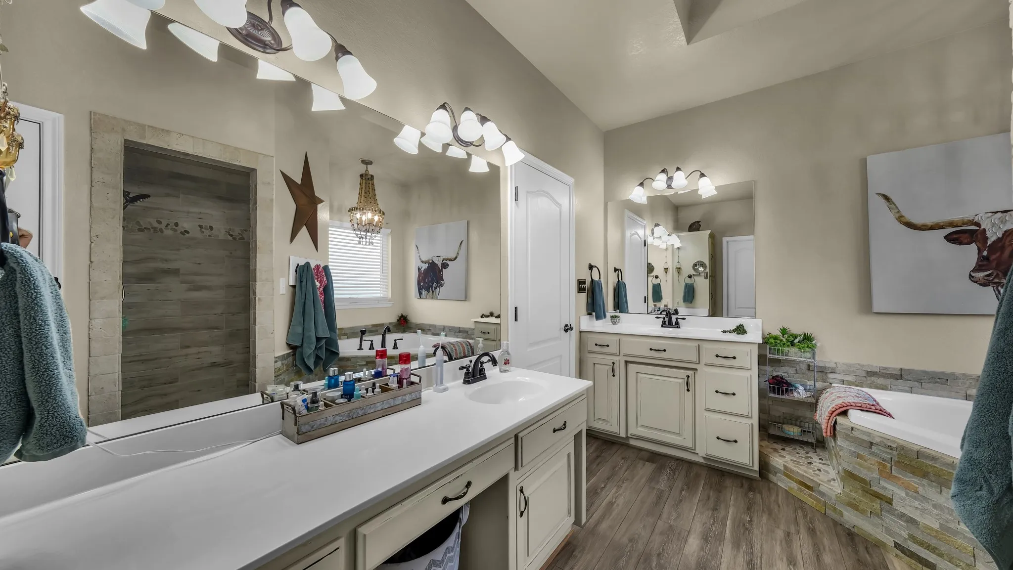 Bathroom featuring dual vanities with white countertops, wood-finish flooring, a tiled soaking tub, and a separate walk-in shower with a stone-look surround