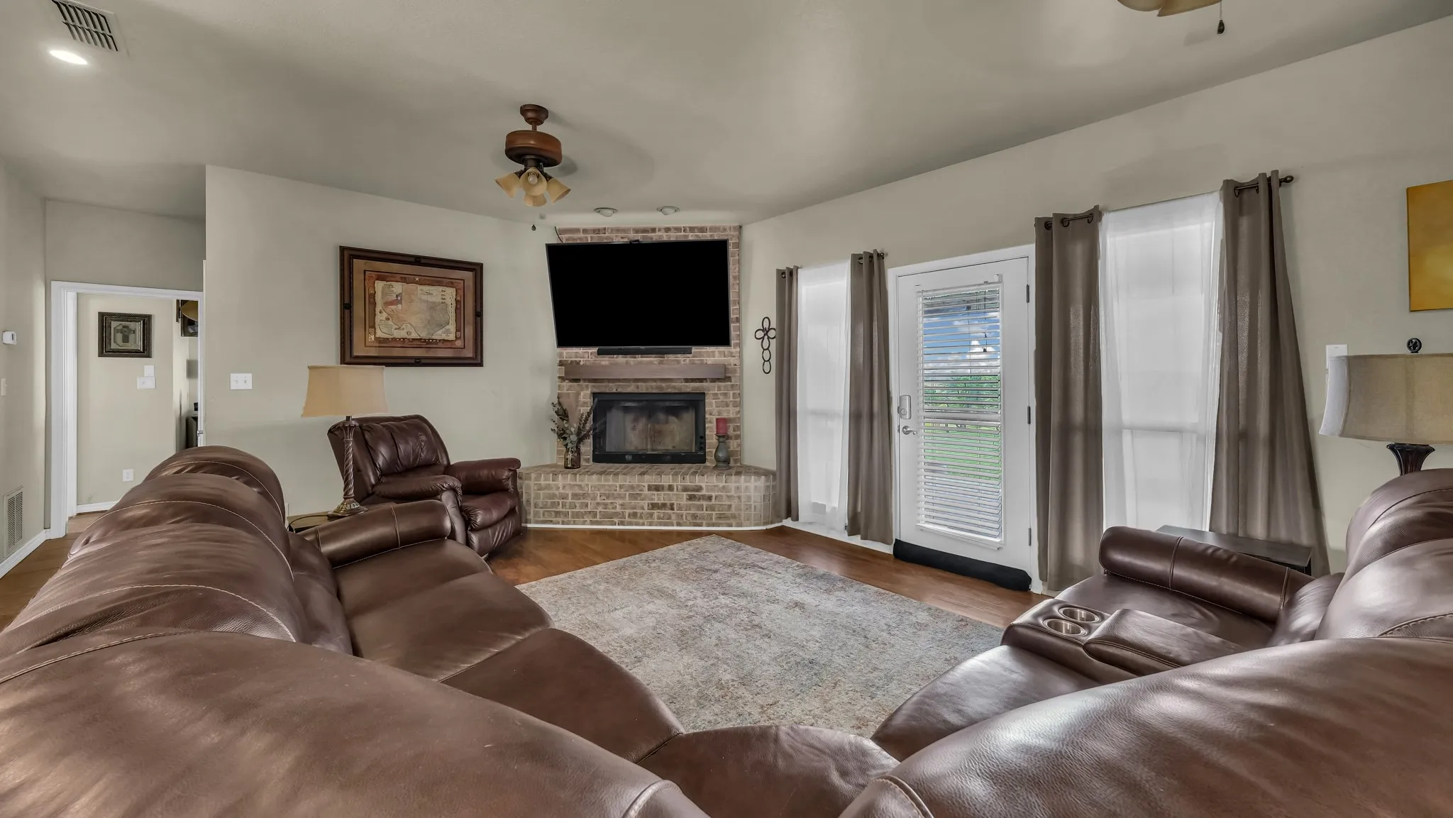 Living space featuring wood-finish flooring and a corner brick fireplace with a wood mantle