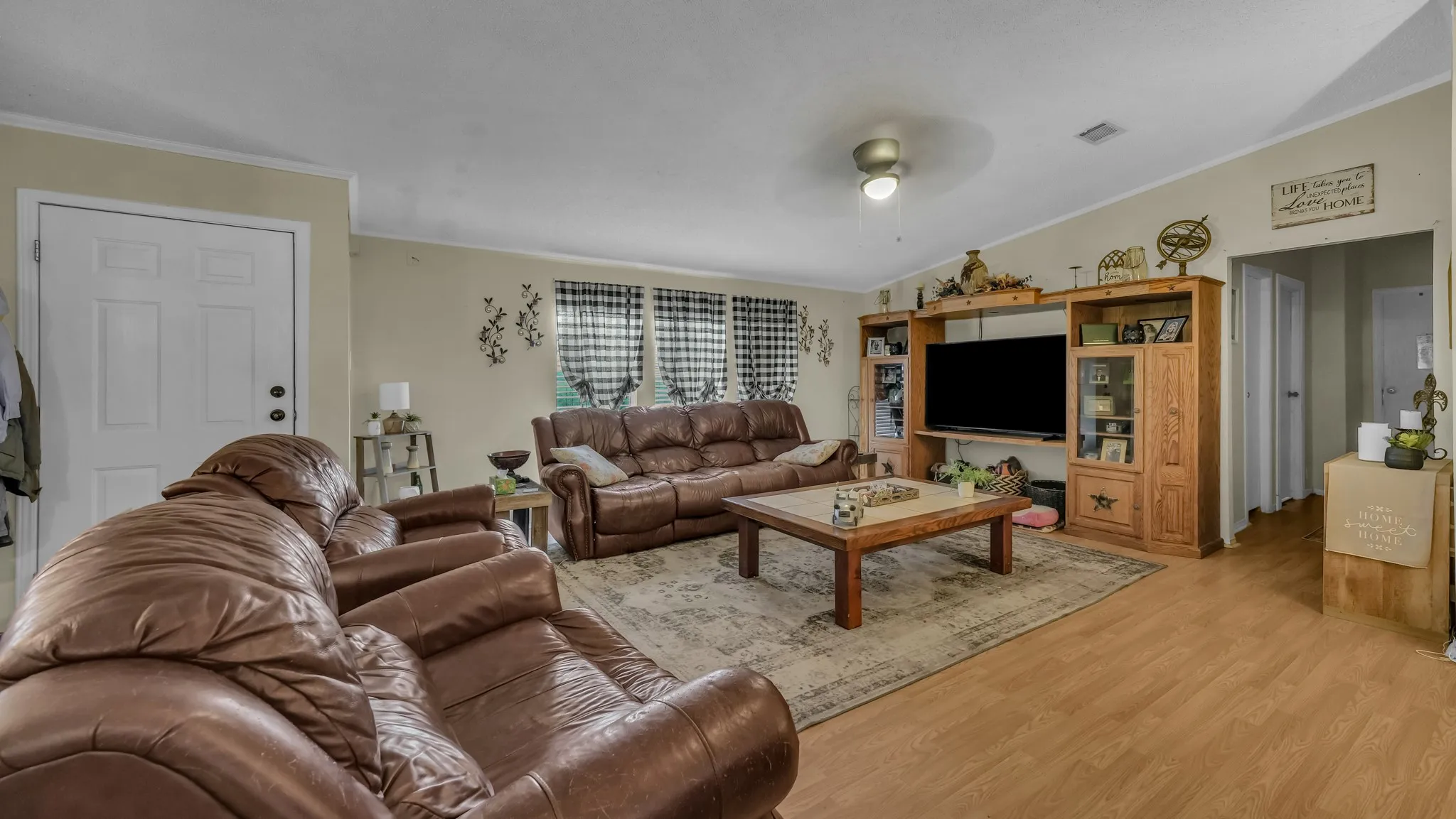 Spacious living room featuring wood-finish flooring, a ceiling fan with integrated lighting, and a built-in entertainment center with shelving and closed storage