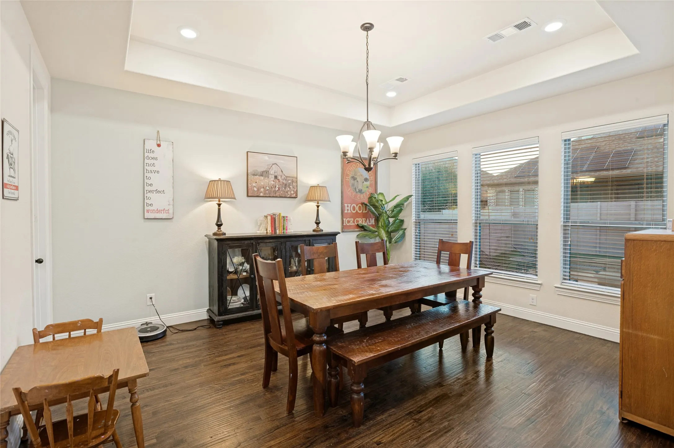 Spacious dining area featuring dark wood-finish flooring, a tray ceiling with recessed lighting, and a multi-light chandelier