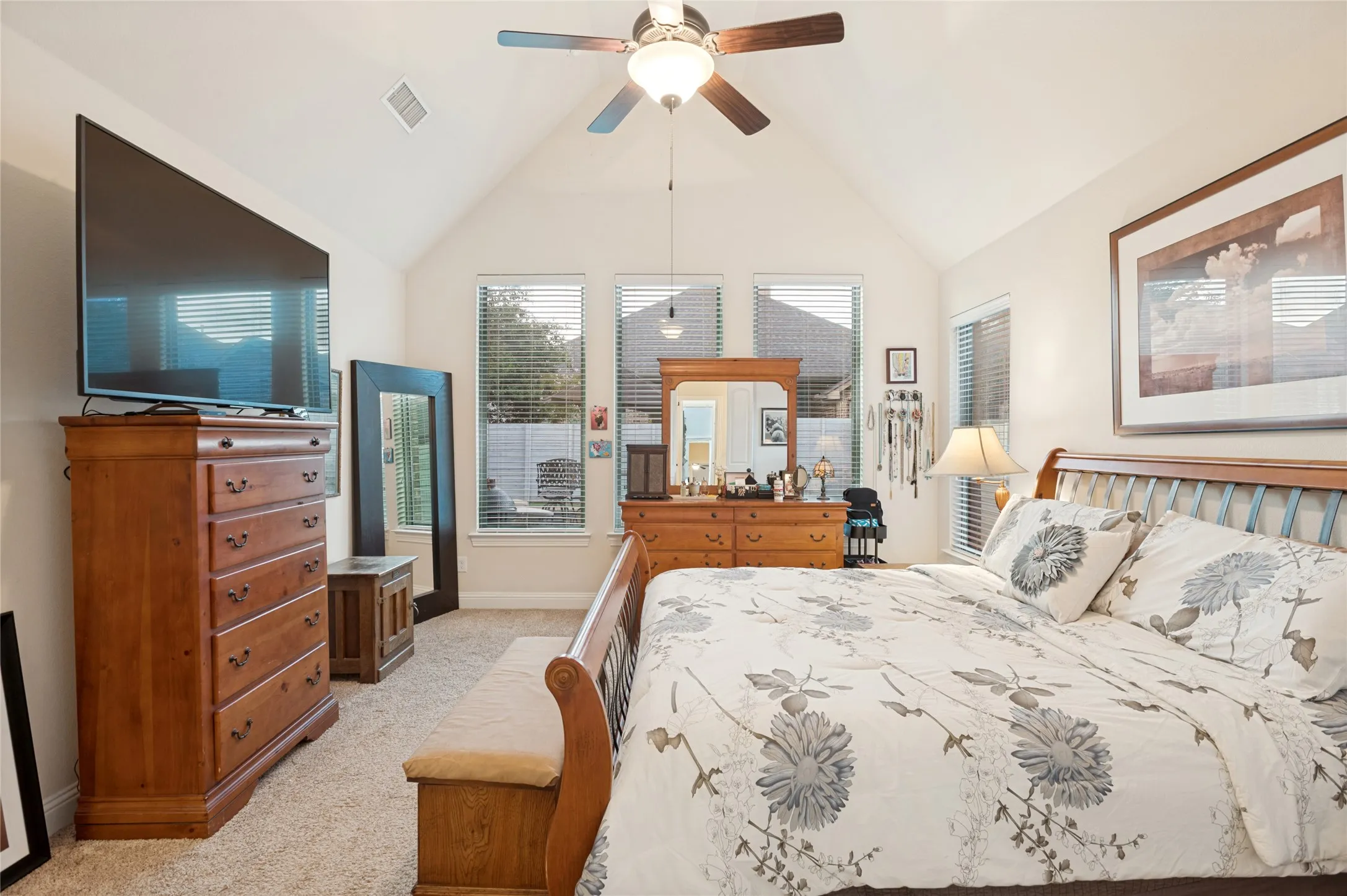 Vaulted ceilings enhance this carpeted bedroom featuring multiple windows with blinds, a ceiling fan with light fixture, and warm-toned wall paint