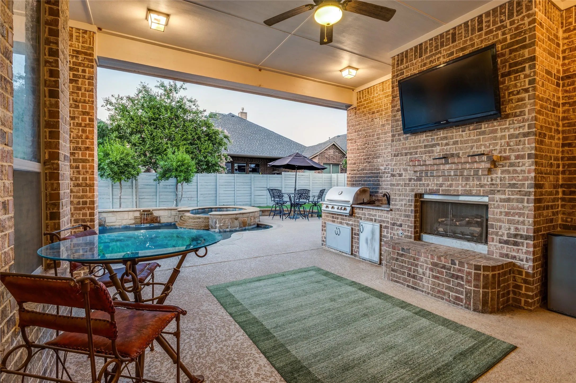 Covered outdoor living space featuring a brick fireplace, built-in grill station, ceiling fan, recessed lighting, and concrete patio