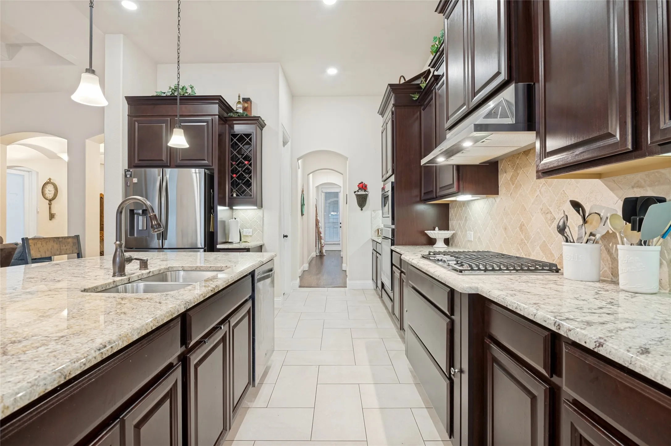Gourmet kitchen featuring dark wood cabinetry, light granite countertops, a tiled backsplash, stainless steel appliances, and recessed lighting