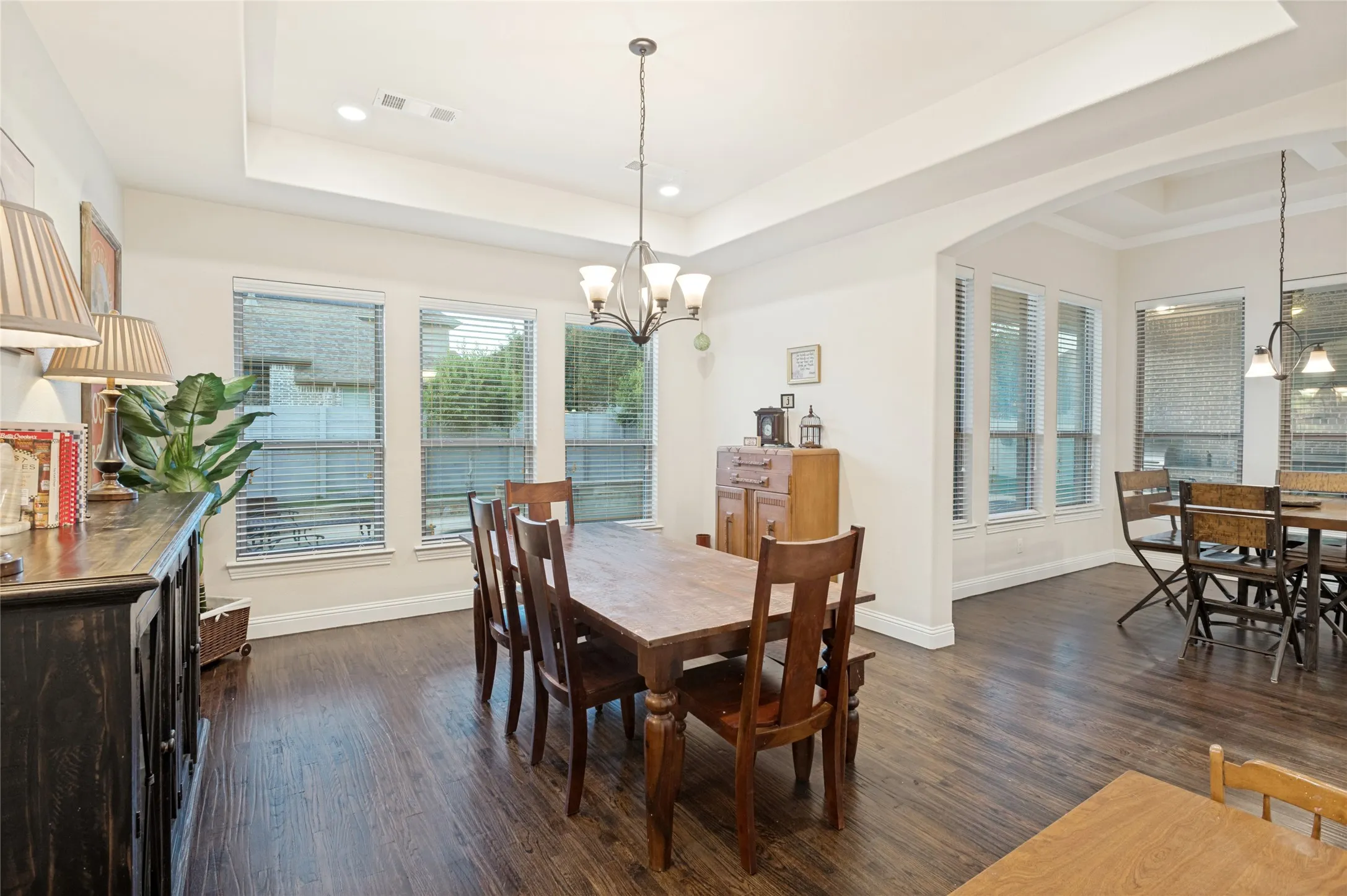 Spacious dining area featuring wood-finish flooring, a tray ceiling with recessed lighting, and a multi-light chandelier