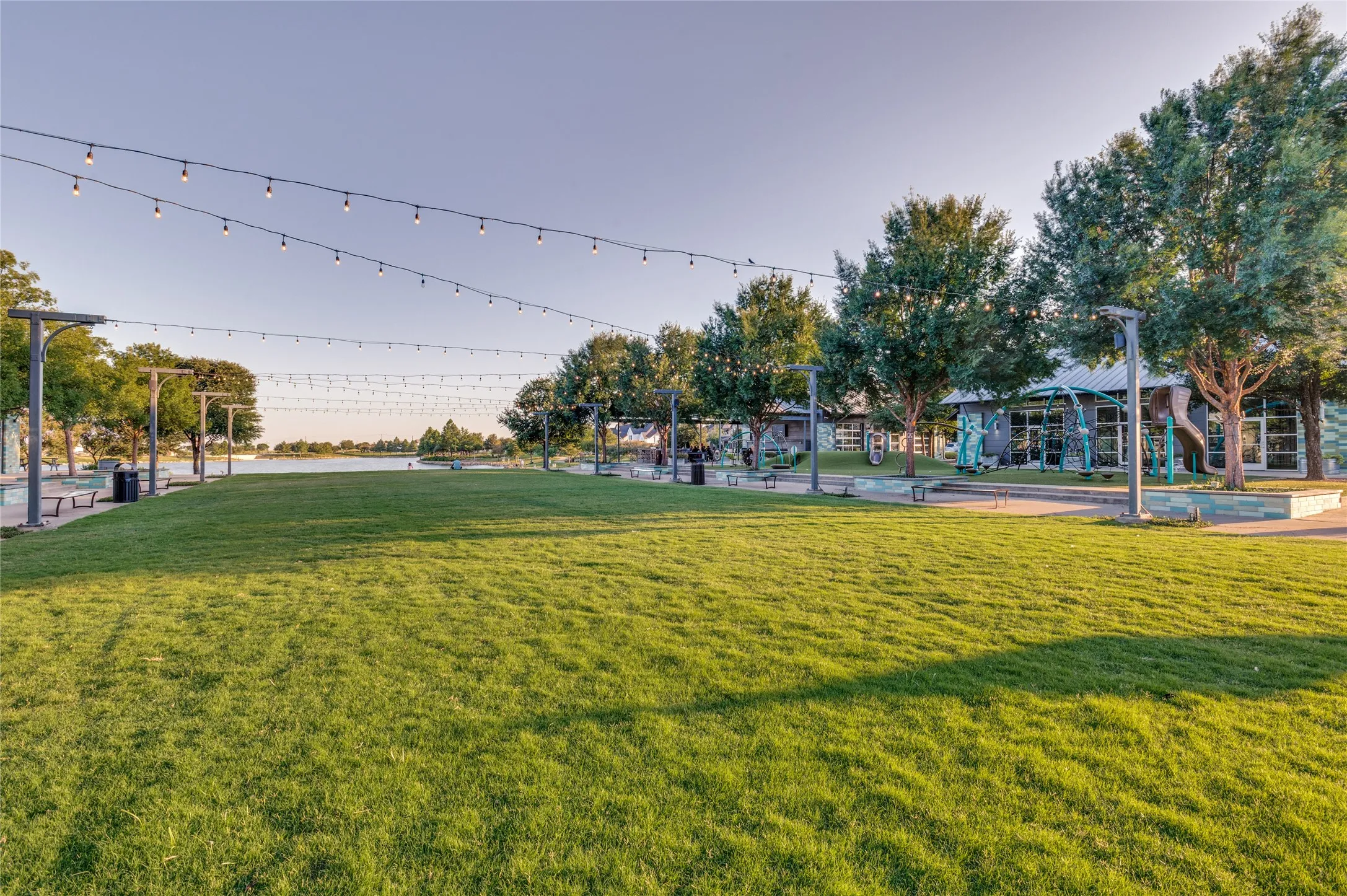 Expansive green space featuring a manicured lawn, established trees, and string lights overhead