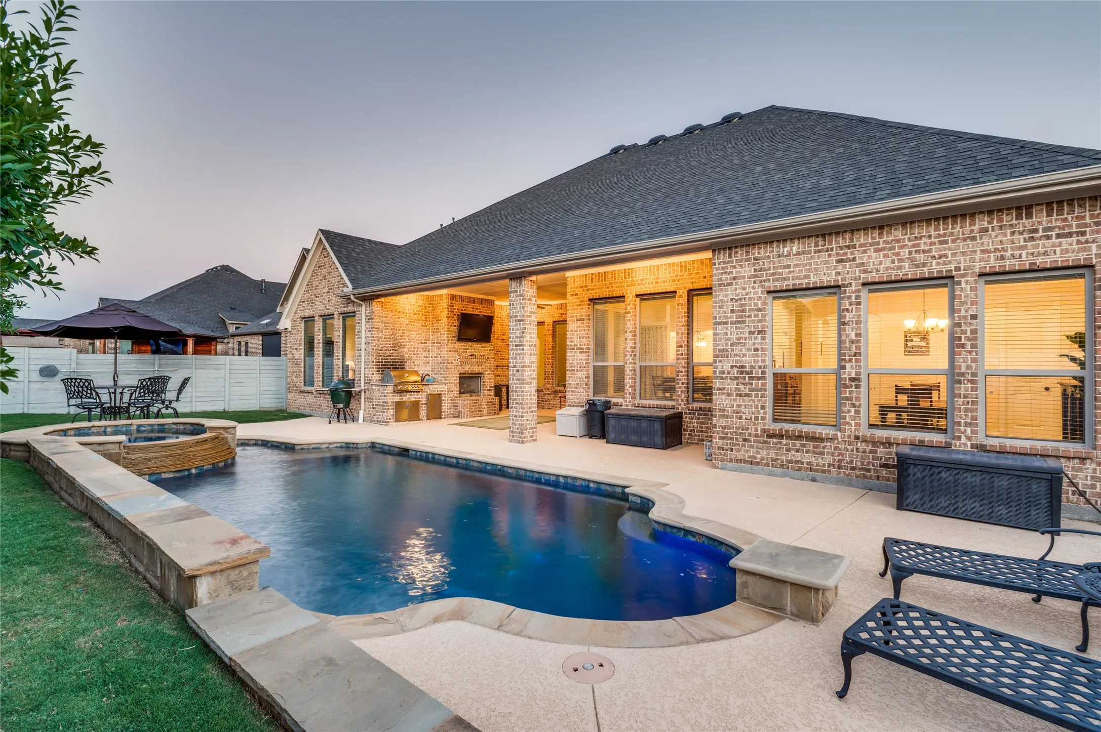 Brick exterior featuring a swimming pool, integrated spa, covered patio, outdoor kitchen, and stone coping