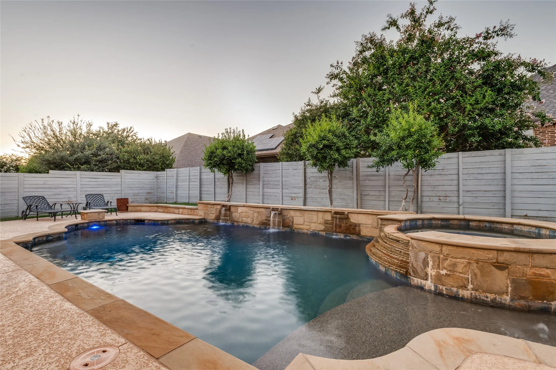 Inviting backyard featuring a swimming pool, stone-clad spa, and perimeter fencing