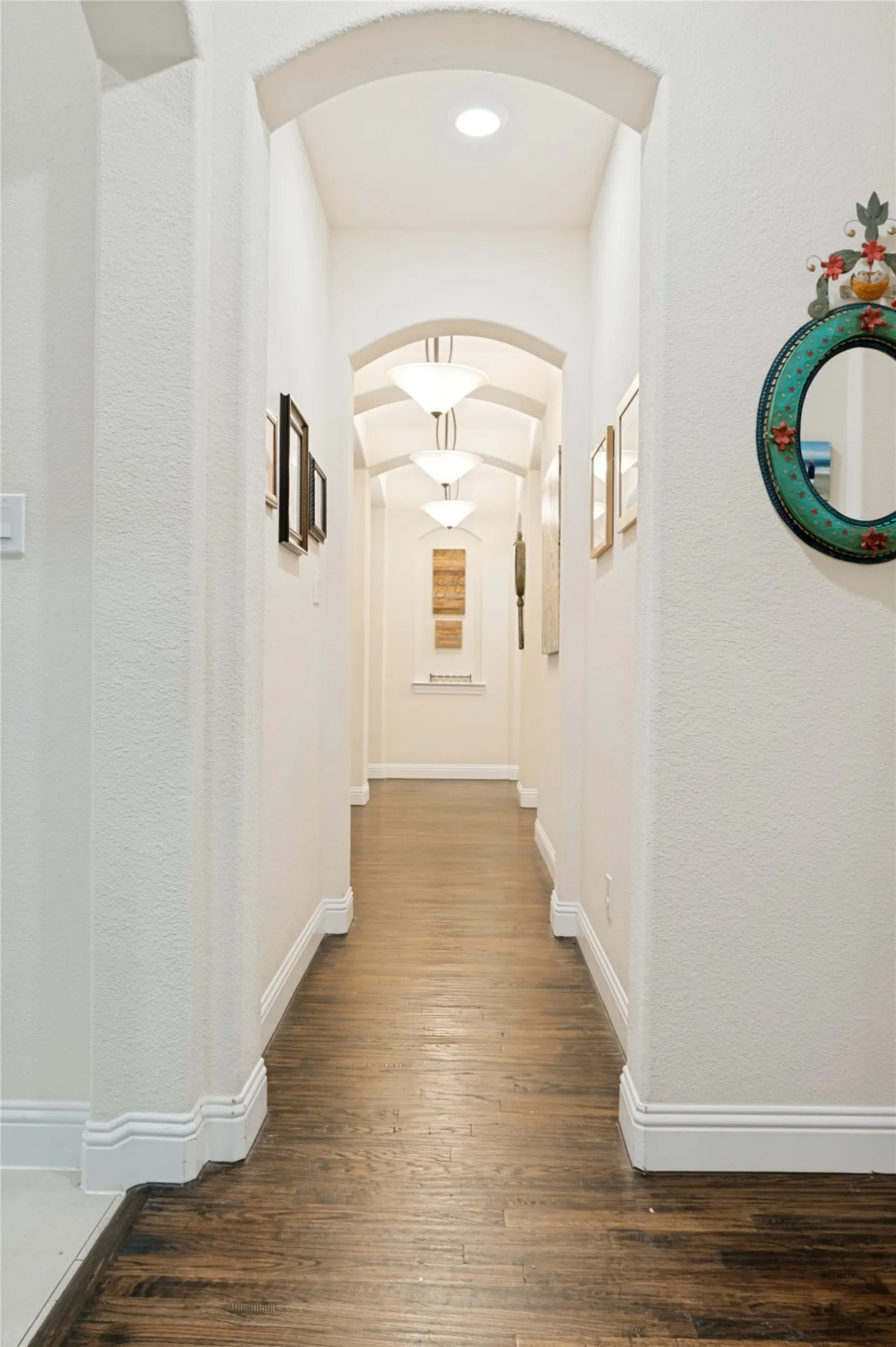 Archway entry to a hallway featuring wood-finish flooring, recessed lighting, and multiple semi-flush mount light fixtures
