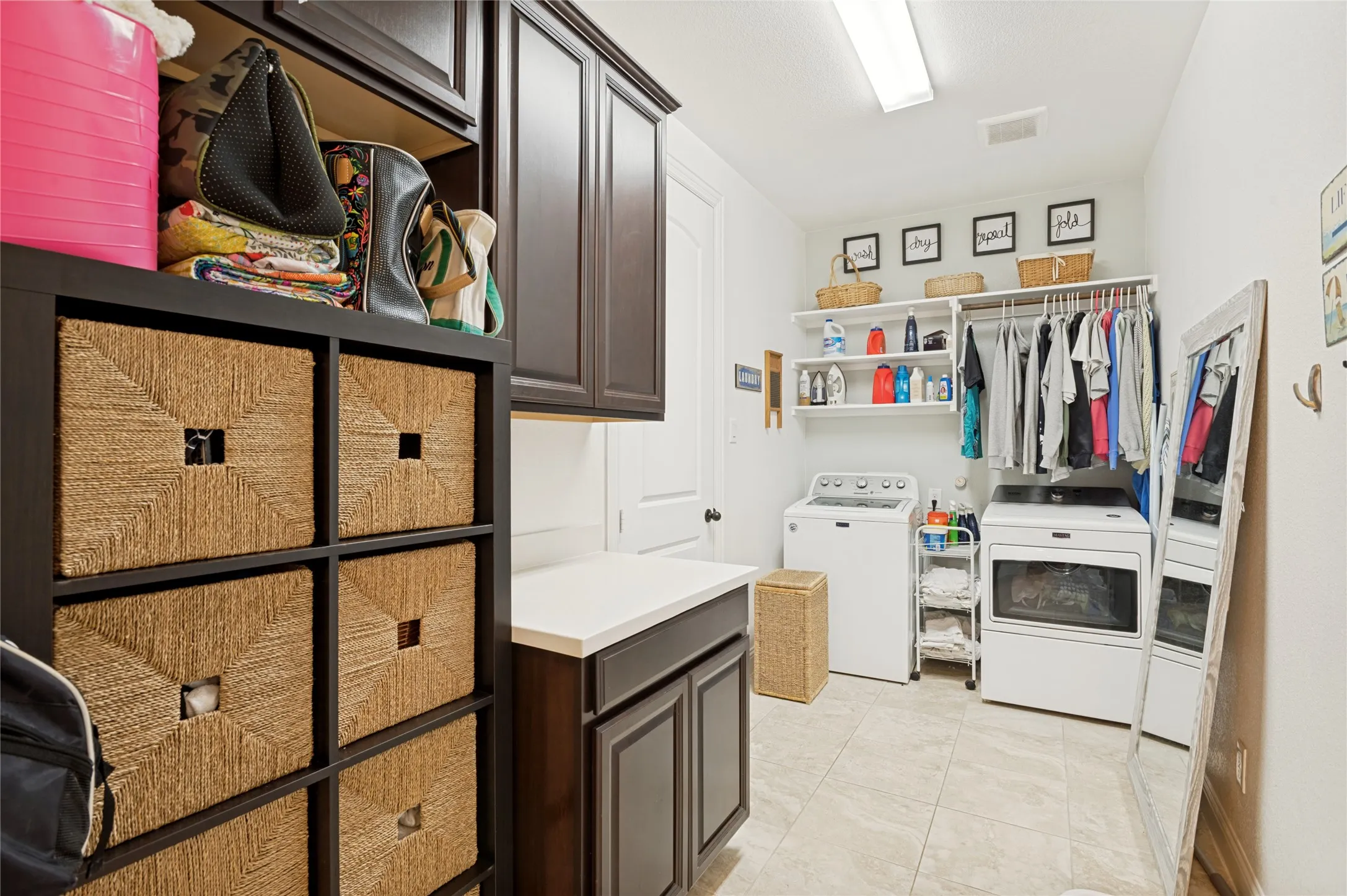 Spacious utility room featuring a built-in folding counter with a light-toned countertop, dark wood-finish cabinetry, and tiled flooring