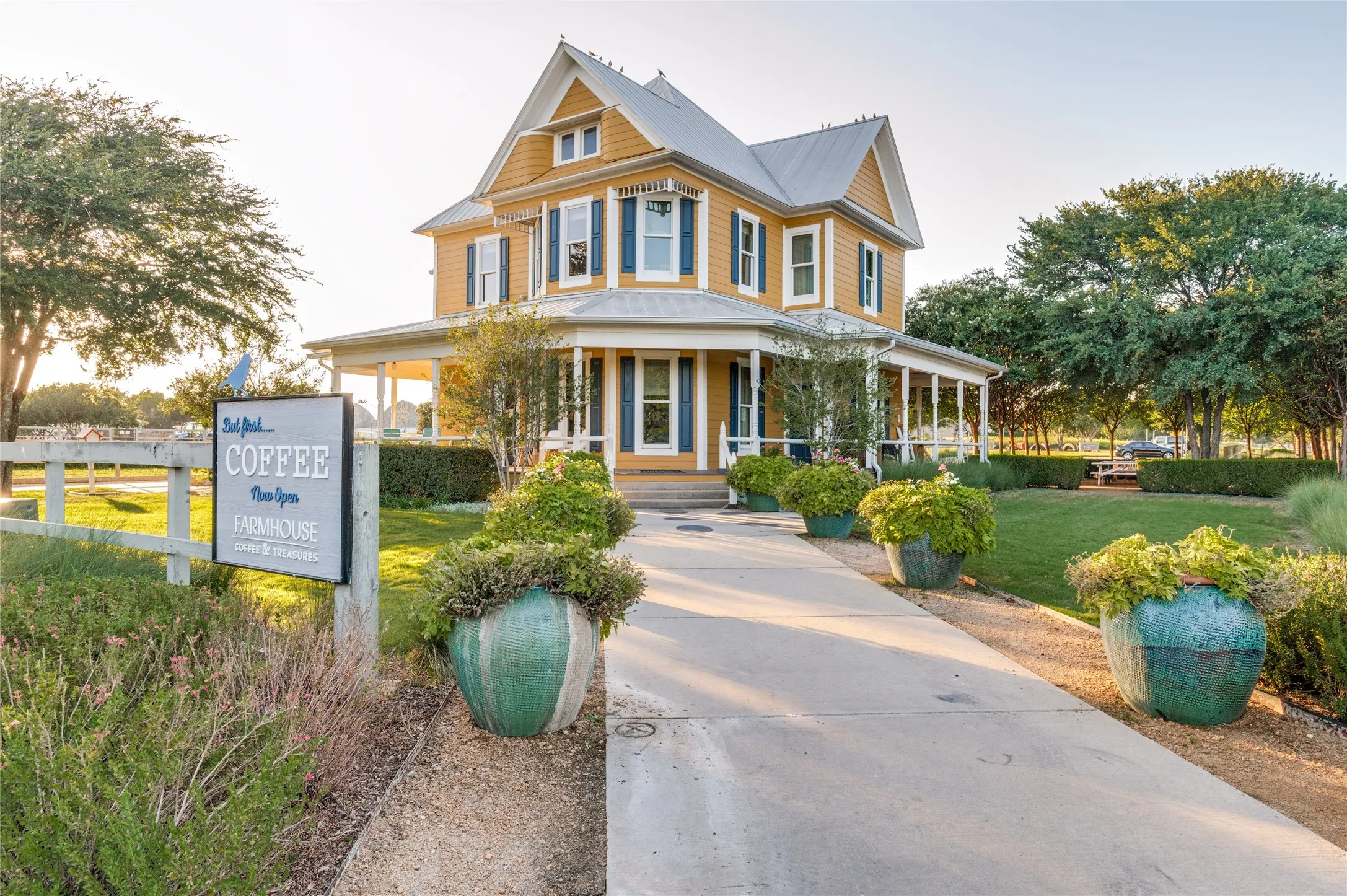 Two-story Victorian-style structure featuring yellow siding, dark blue window shutters, a covered wraparound porch, and a light gray metal roof