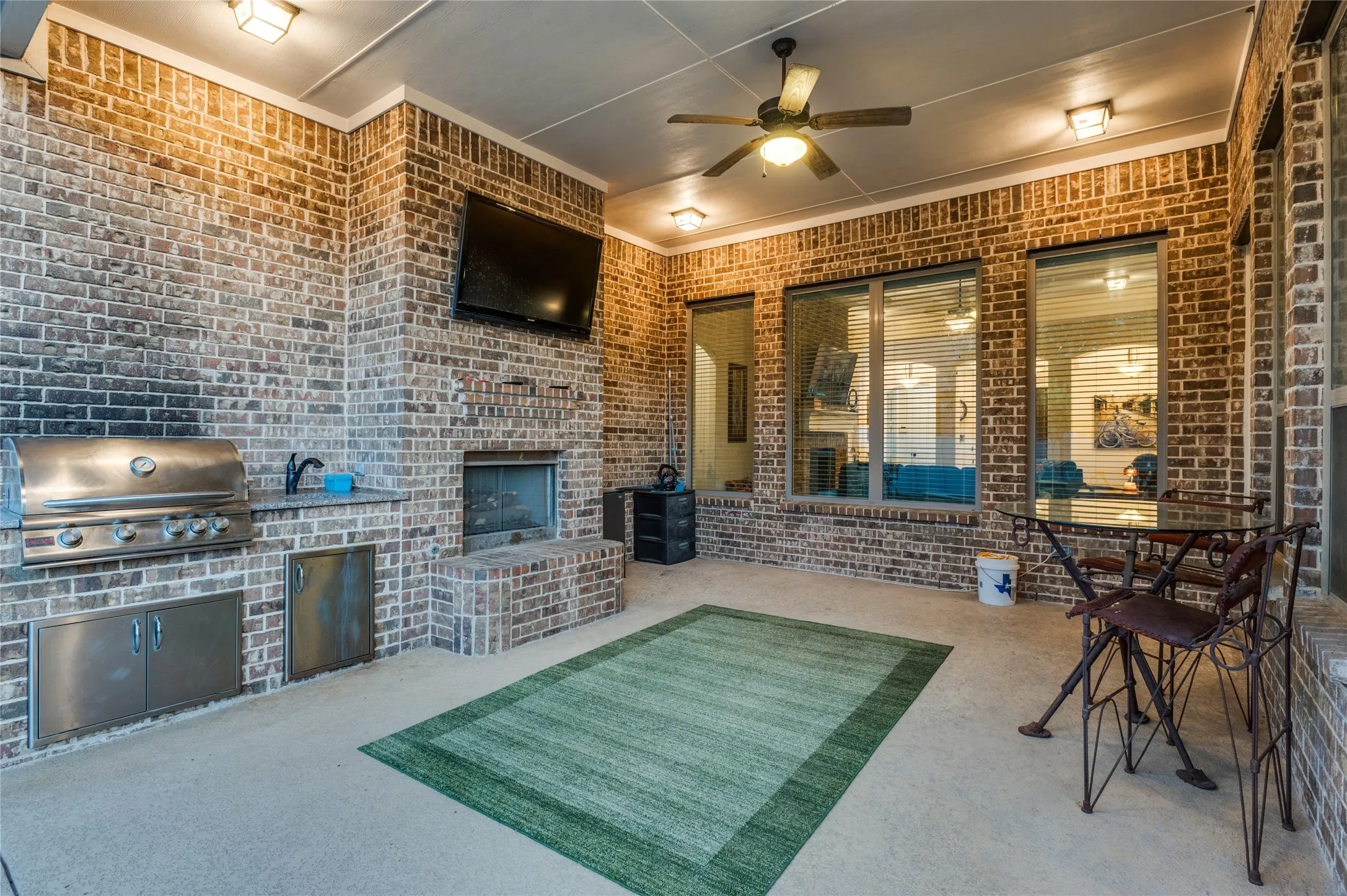 Covered outdoor patio featuring a built-in brick fireplace, integrated stainless steel grill, and an outdoor ceiling fan