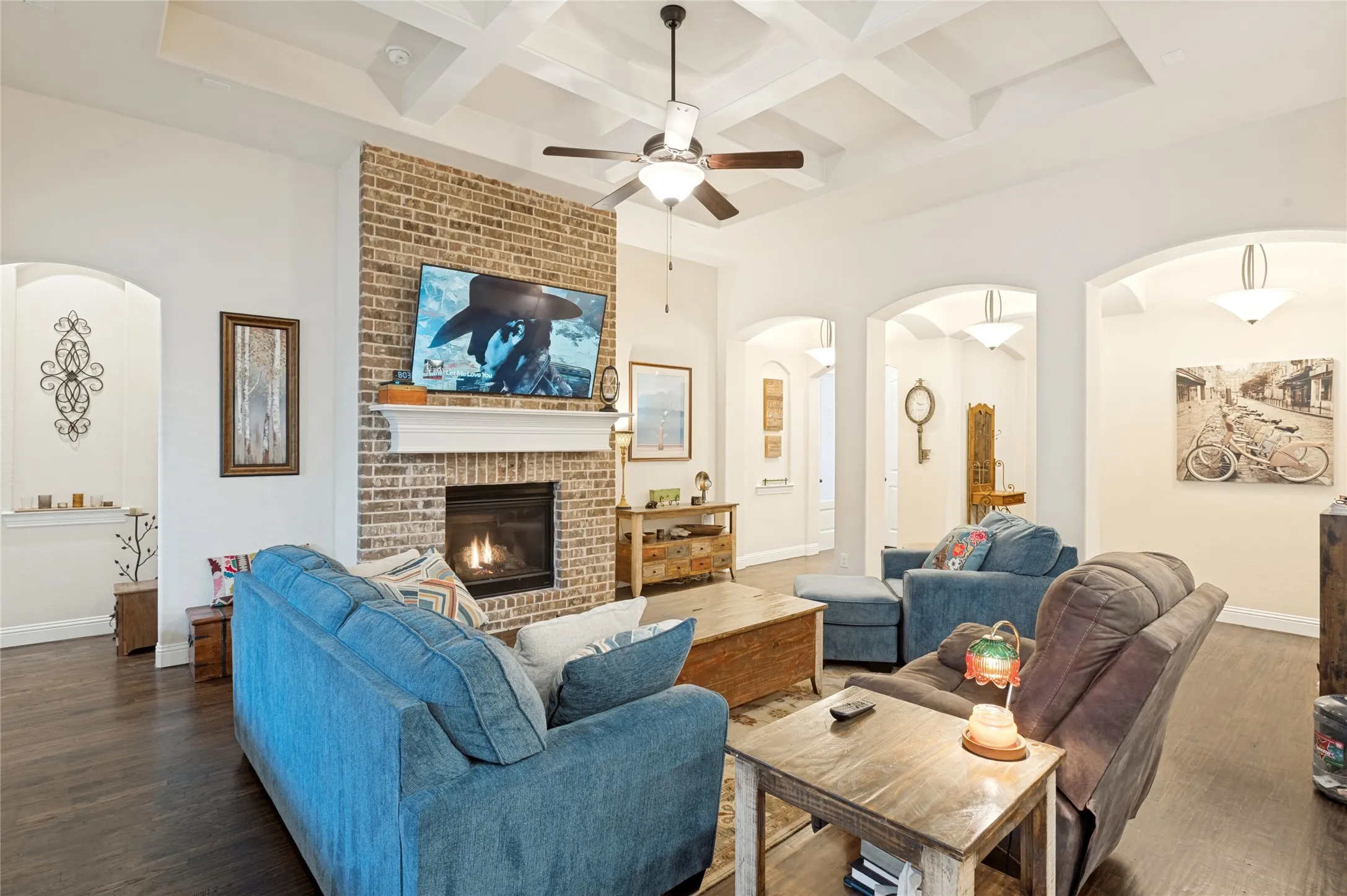 Spacious living area featuring a brick fireplace with a white mantel, coffered ceilings, and dark wood-finish flooring