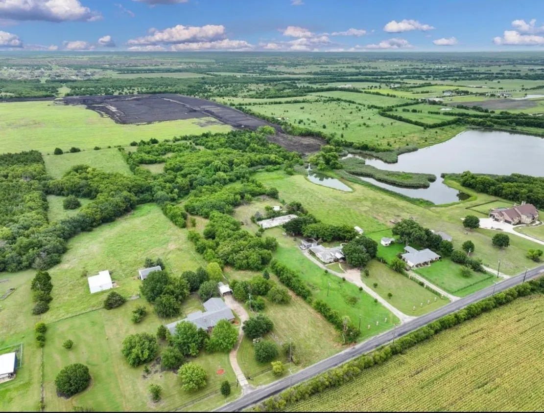 Expansive rural landscape featuring a large body of water, scattered residences, agricultural fields, and wooded areas