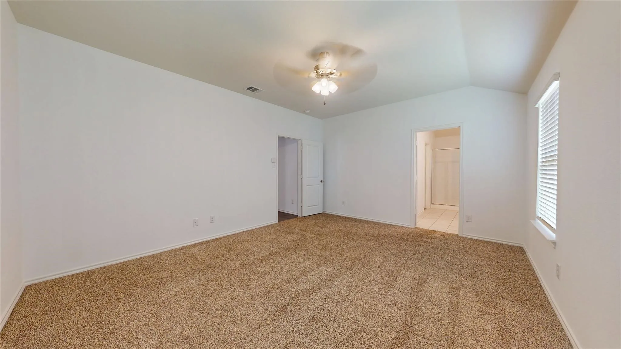 Spacious carpeted room featuring a vaulted ceiling with a flush-mount ceiling fan, white painted walls, and a window with blinds