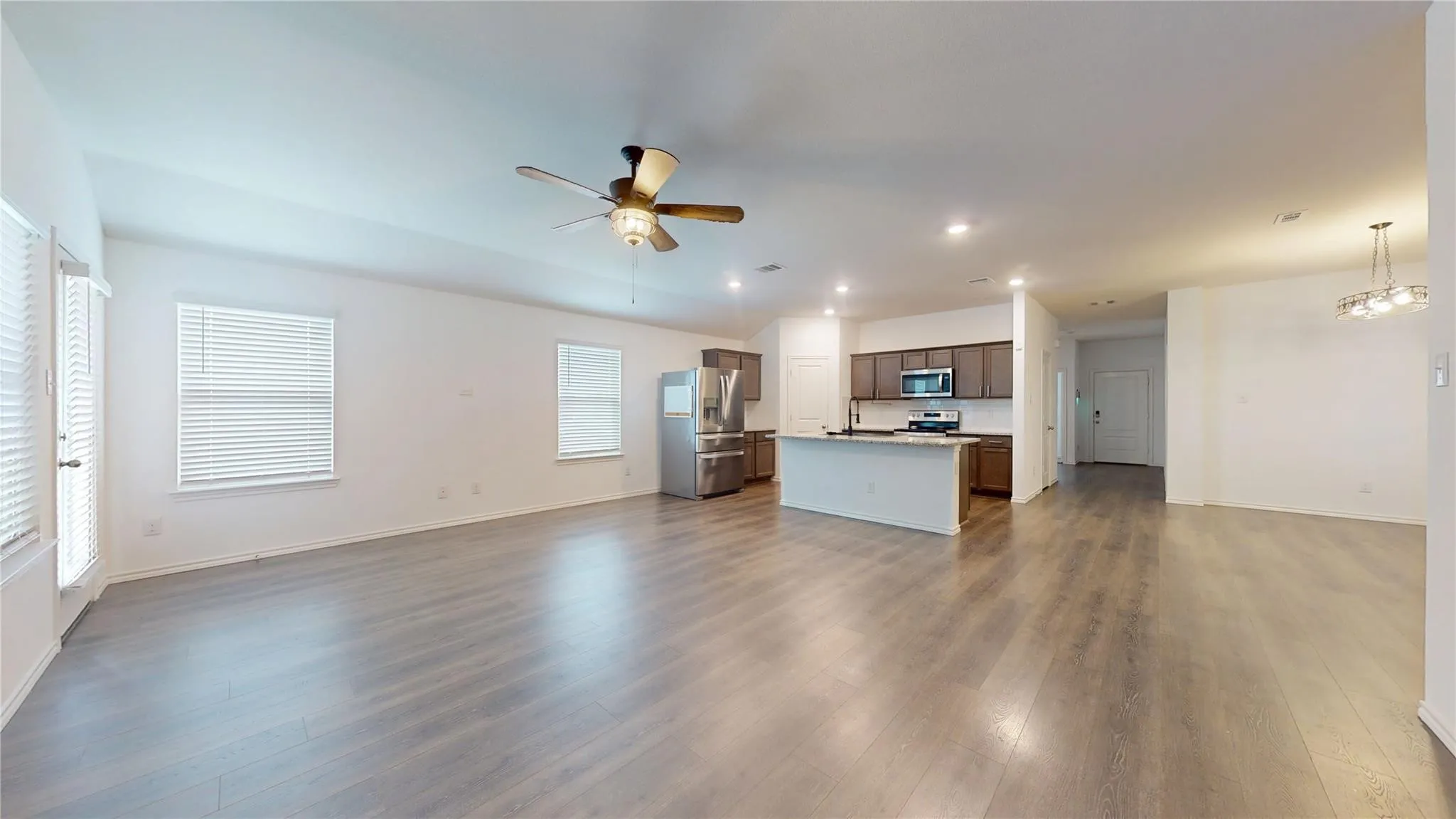 Expansive open-concept living space featuring wood-finish flooring throughout, a modern ceiling fan, and recessed lighting