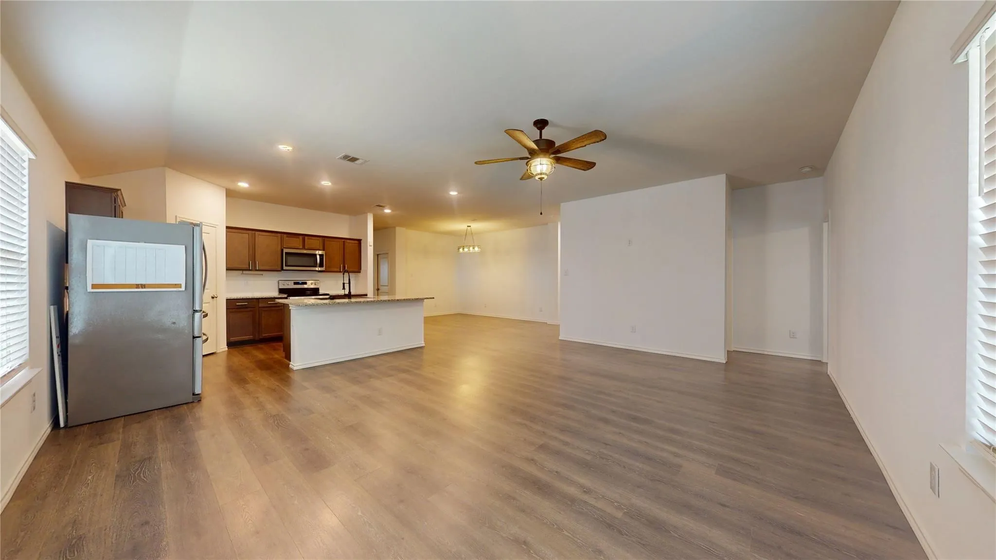 Spacious open-concept living area featuring wood-finish flooring, a kitchen island with seating, dark wood cabinetry, and a ceiling fan