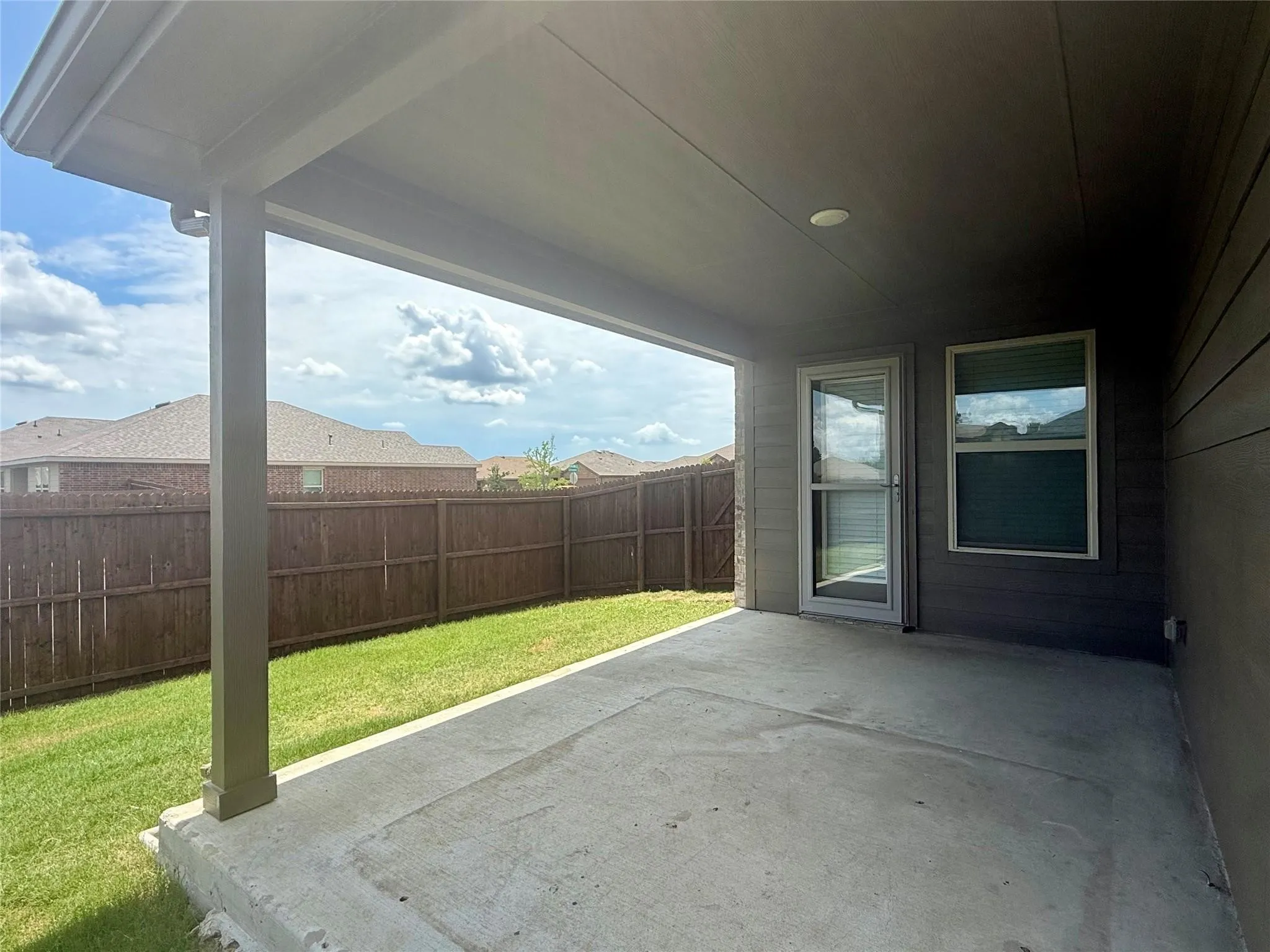 Covered concrete patio extending into a grassed yard, bordered by a privacy fence