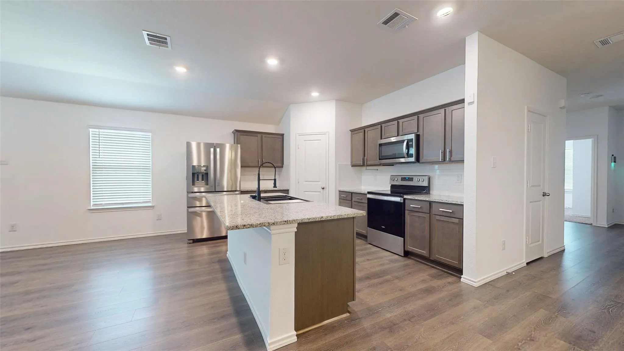 Modern kitchen featuring an island with a light-toned countertop, stainless steel appliances, dark wood-finish cabinetry, and a white subway tile backsplash