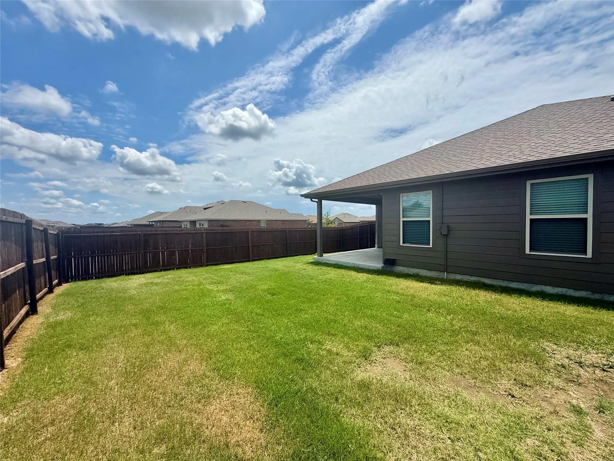 Expansive backyard featuring a covered patio, privacy fencing, and a large grass lawn