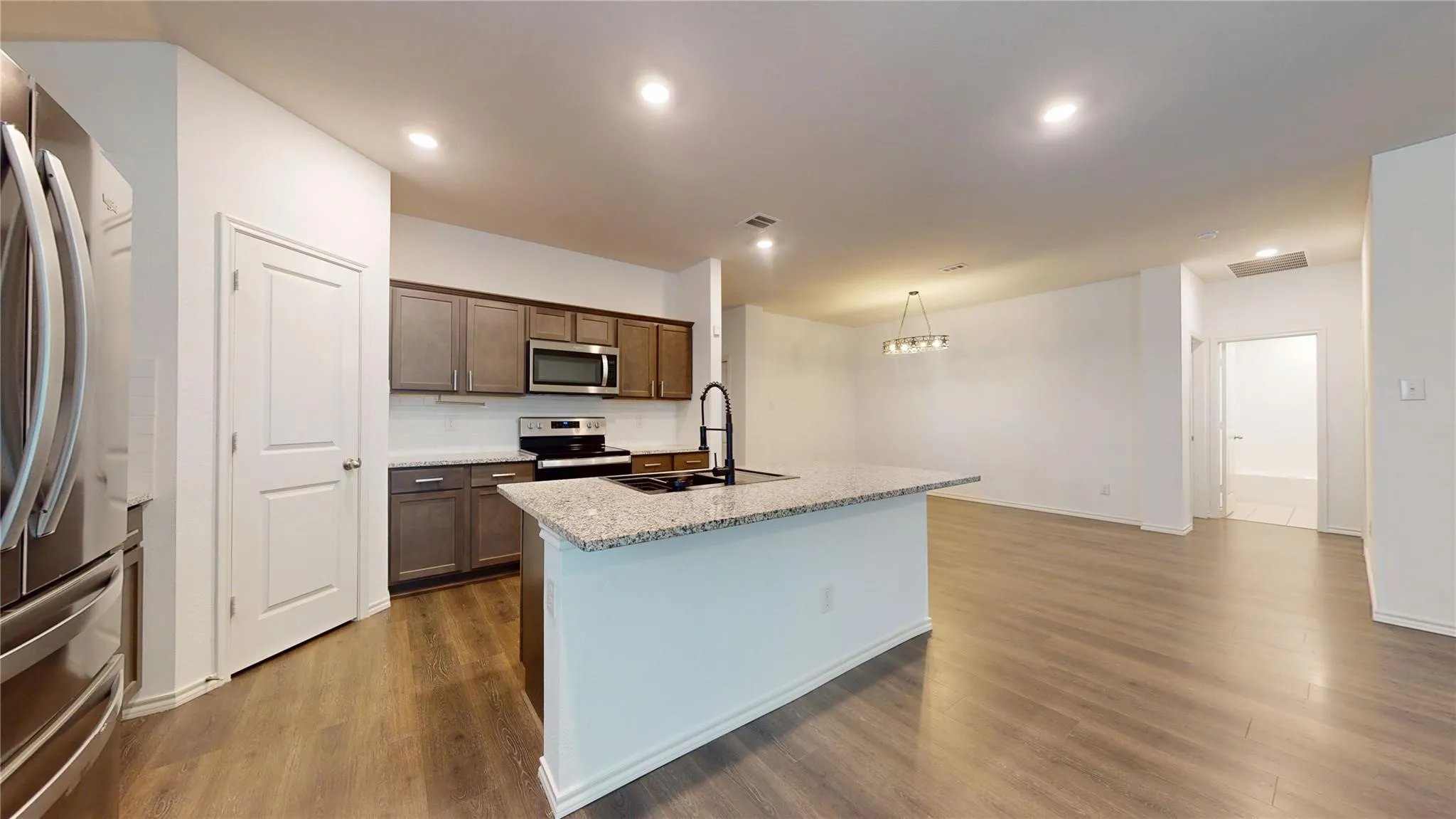 Open-concept kitchen and dining area featuring a spacious island with a stone-finish countertop, dark wood-finish cabinetry, stainless steel appliances, and wood-finish flooring