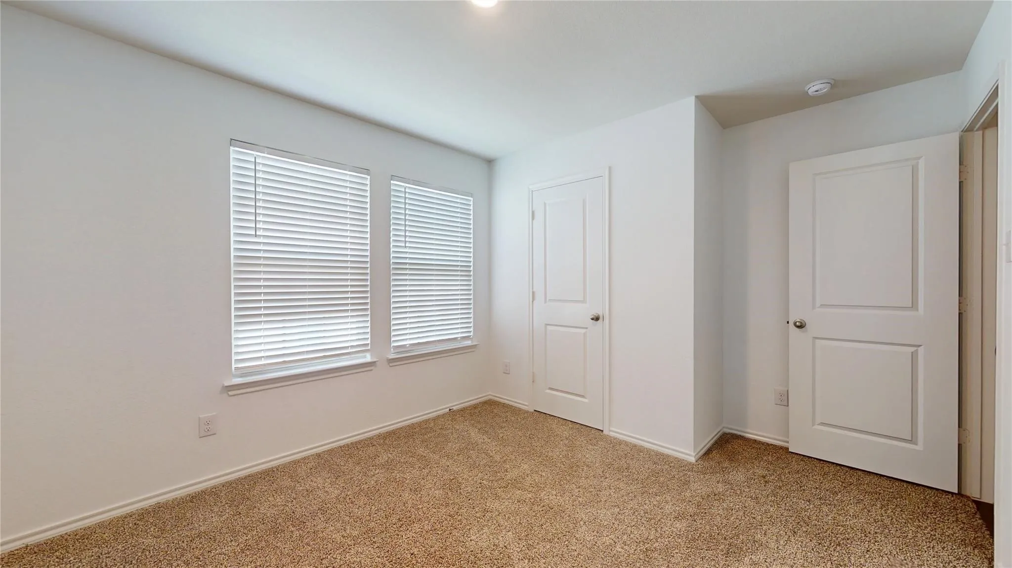 Carpeted room with white walls, two windows featuring horizontal blinds, and two panel doors with chrome hardware