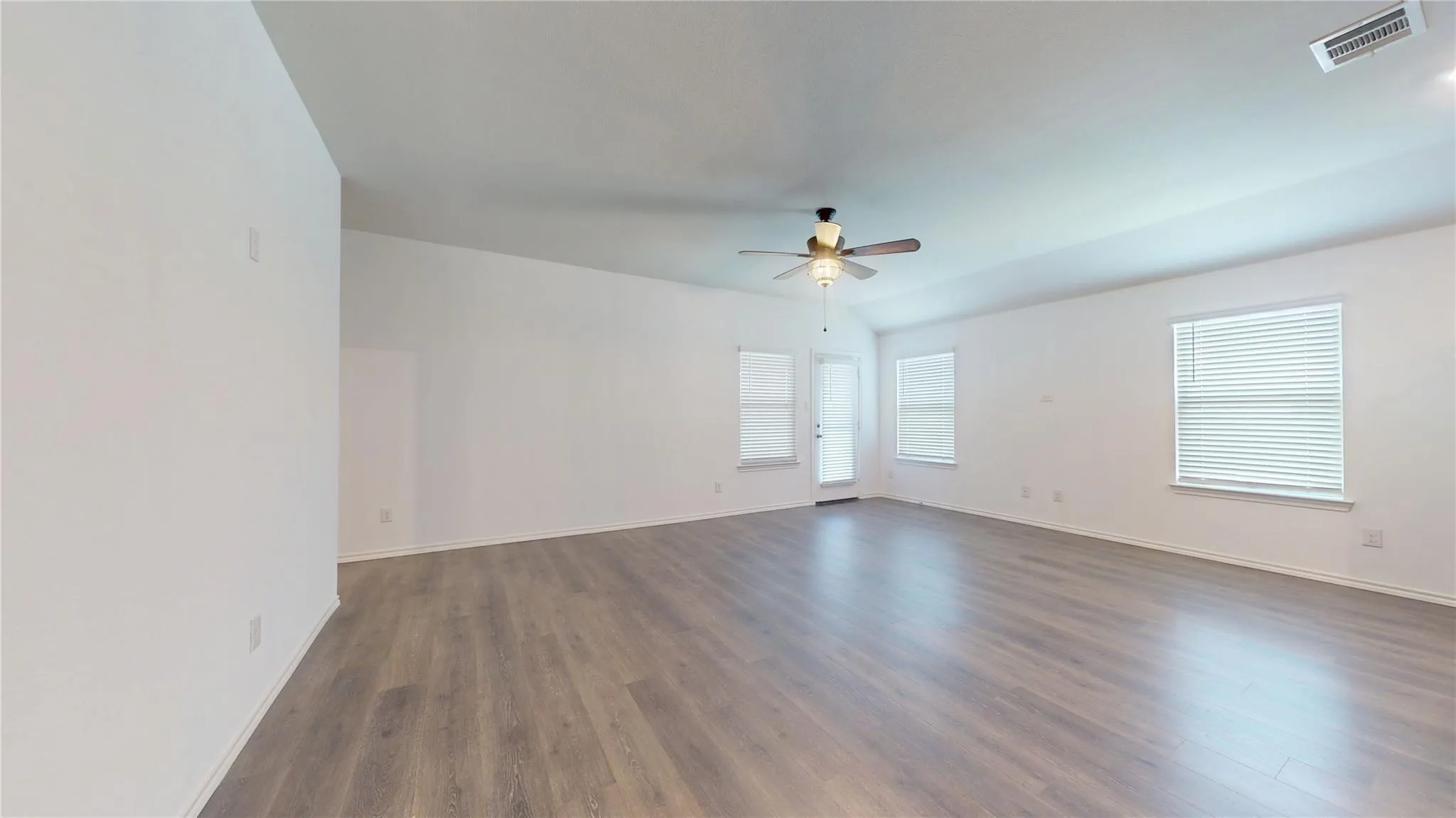 Spacious room featuring vaulted ceilings, light wood-finish flooring, and crisp white walls