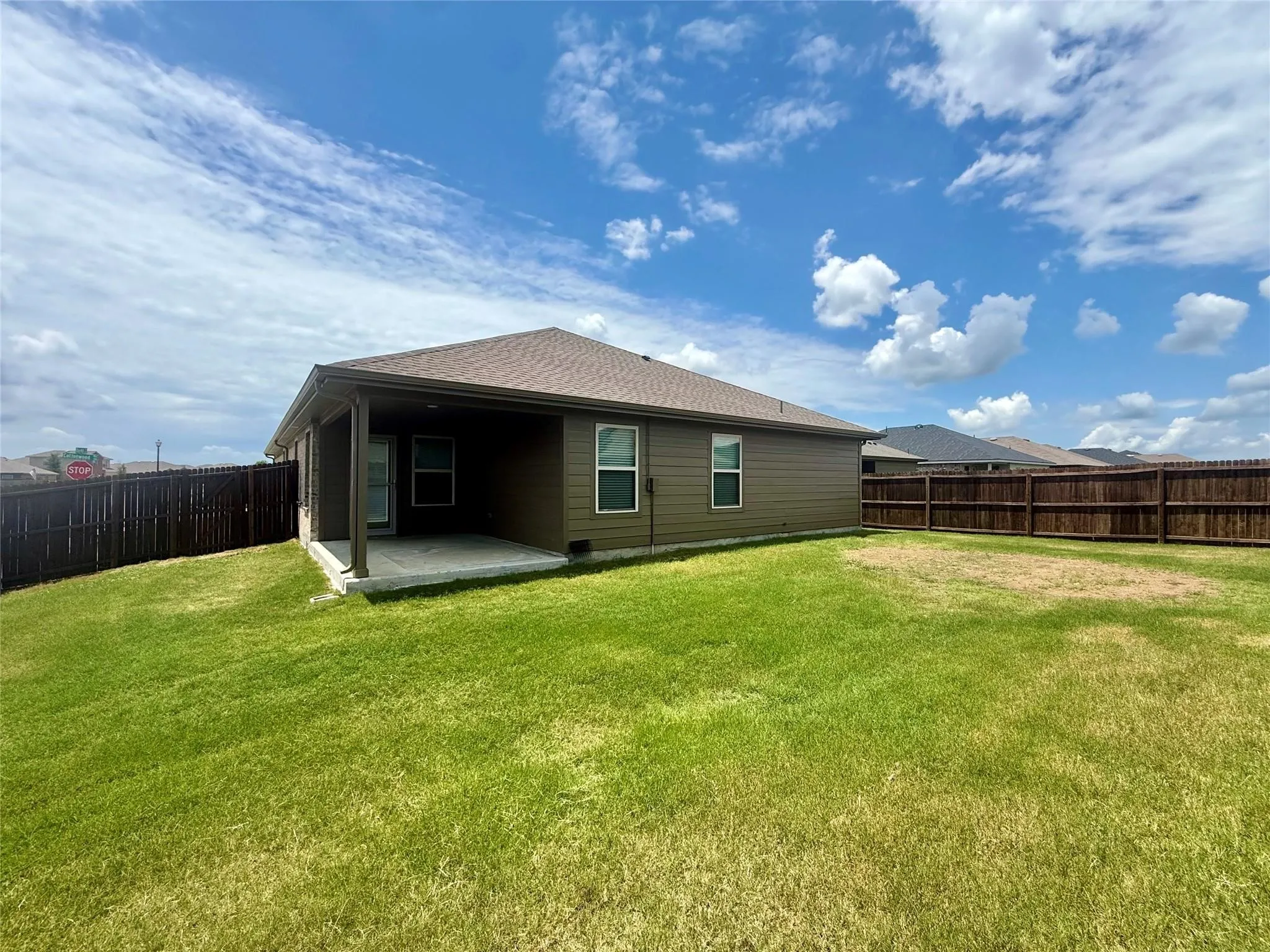 Expansive backyard featuring a covered patio, privacy fencing, and a large grass lawn