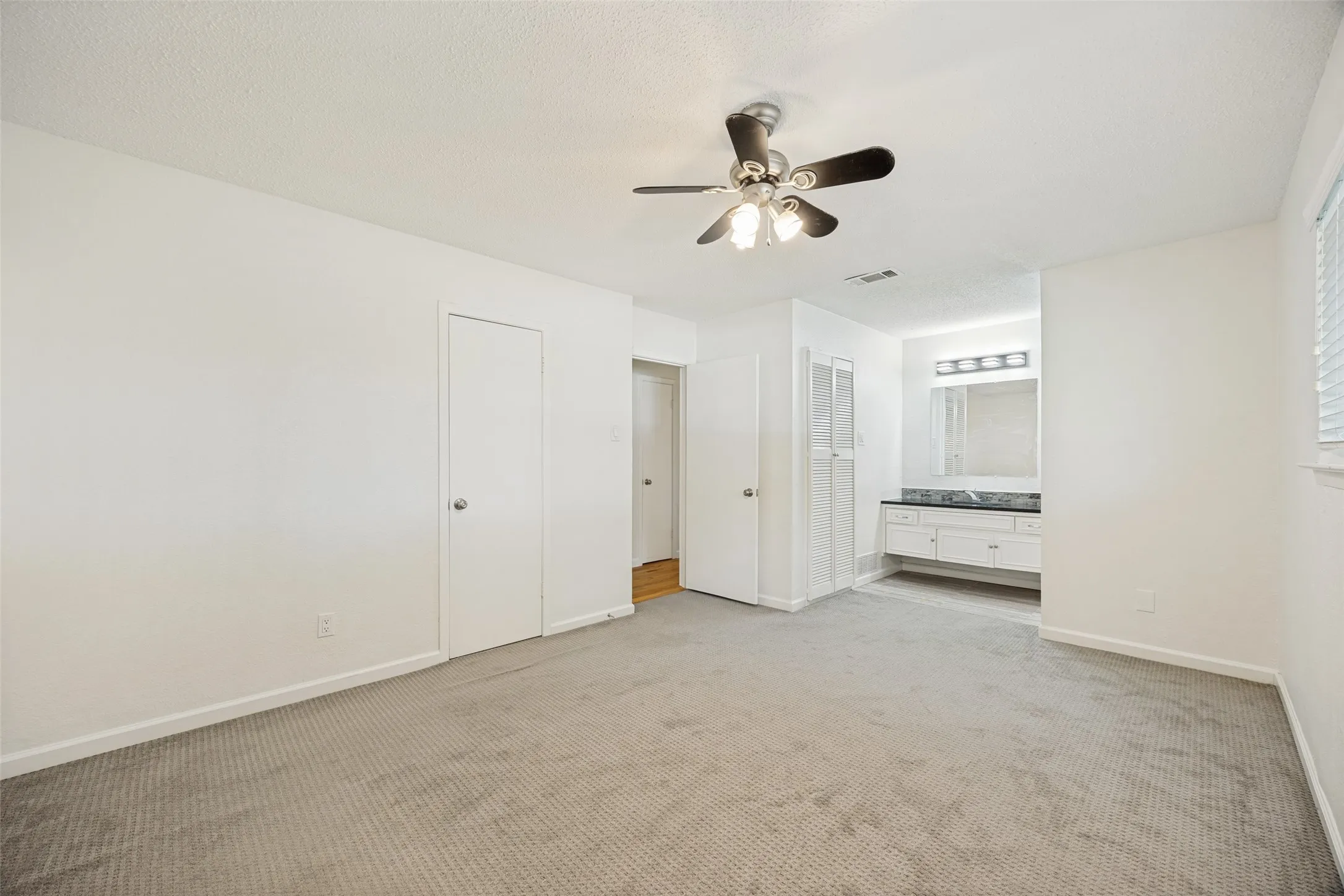 Spacious carpeted room featuring a ceiling fan with light fixture, window with blinds, and white painted walls
