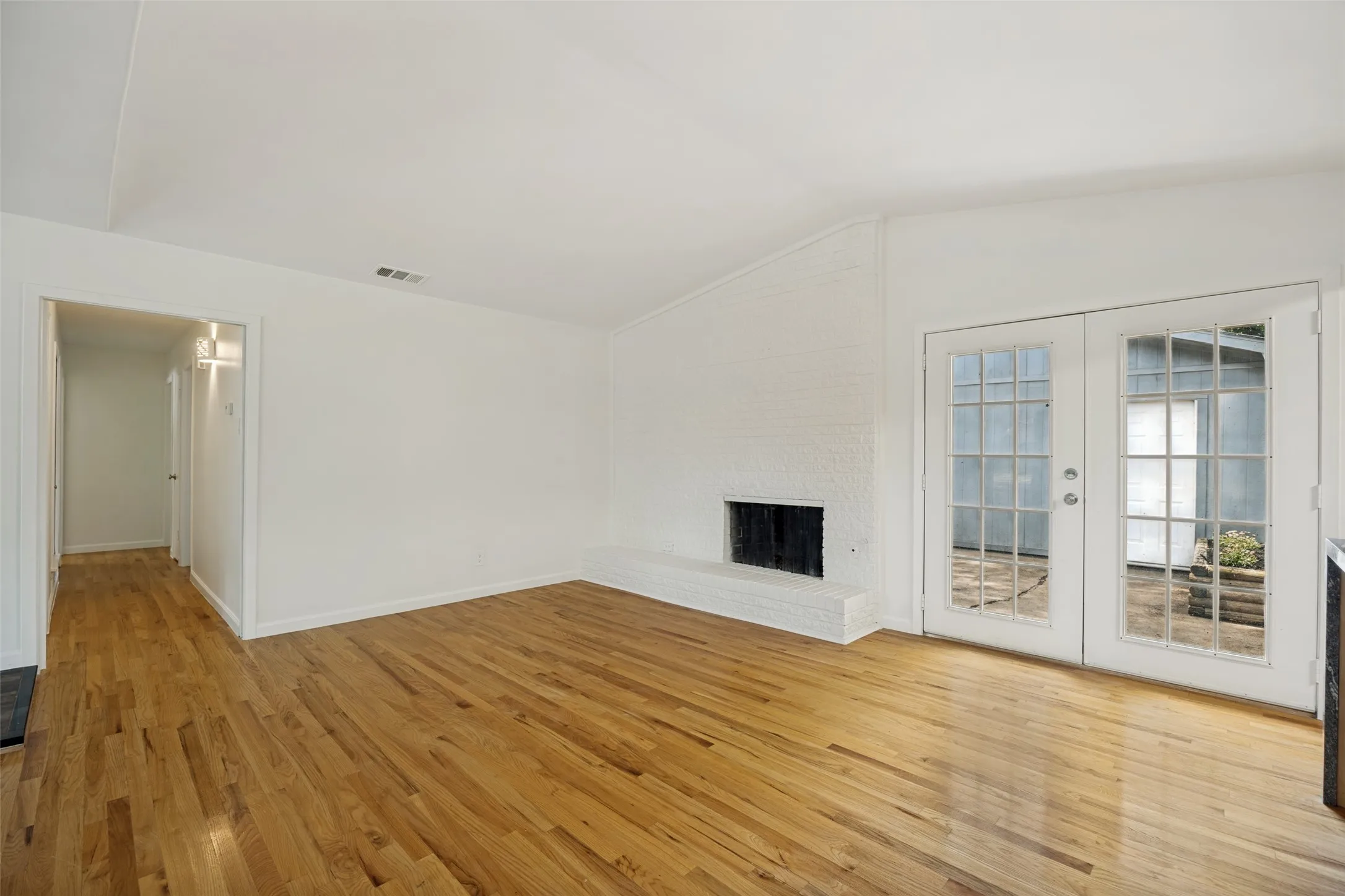 Spacious interior featuring wood-finish flooring, a white brick fireplace, and double glass-paned doors