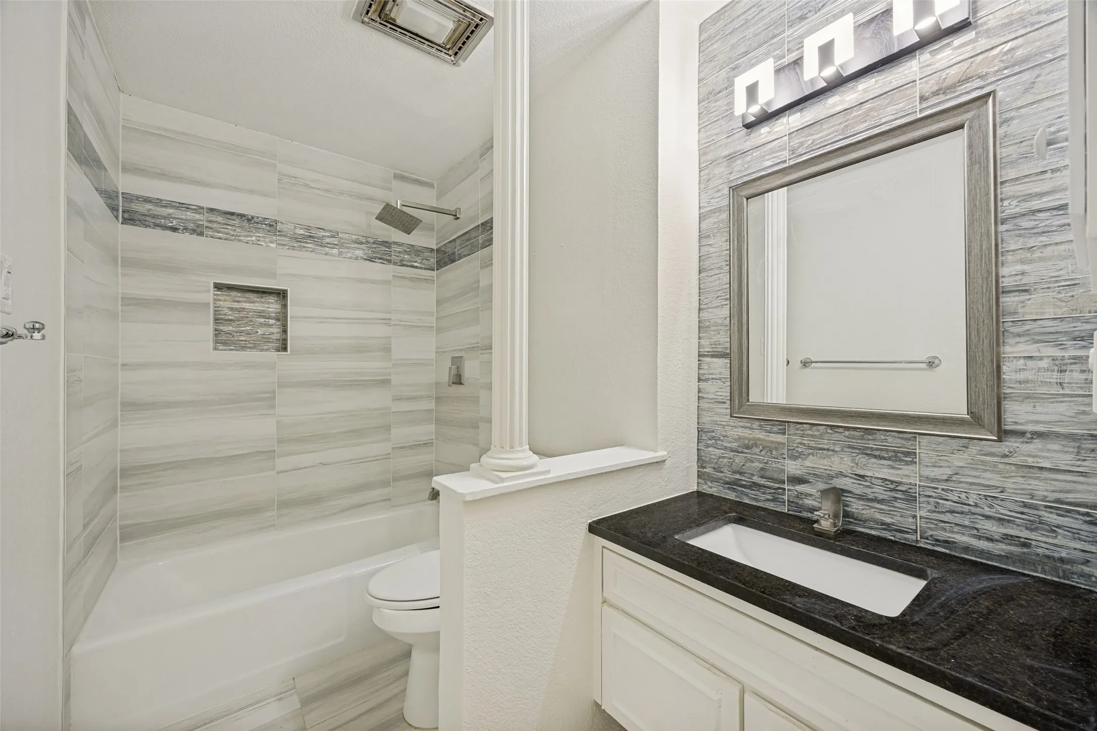 Bathroom featuring a vanity with a dark countertop and integrated sink, a large framed mirror, and a modern light fixture